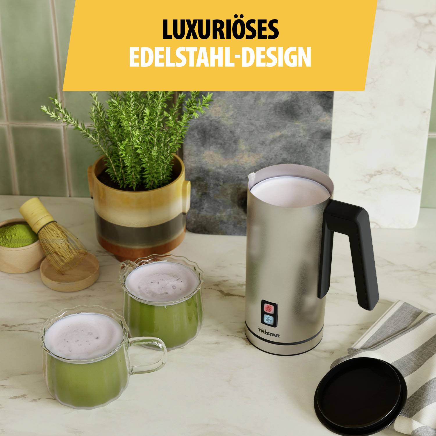 Strieborná kanvica na kuchynskom stole s dvoma šálkami matcha. Rastlina v pozadí. Text: Luxusný dizajn z nehrdzavejúcej ocele.