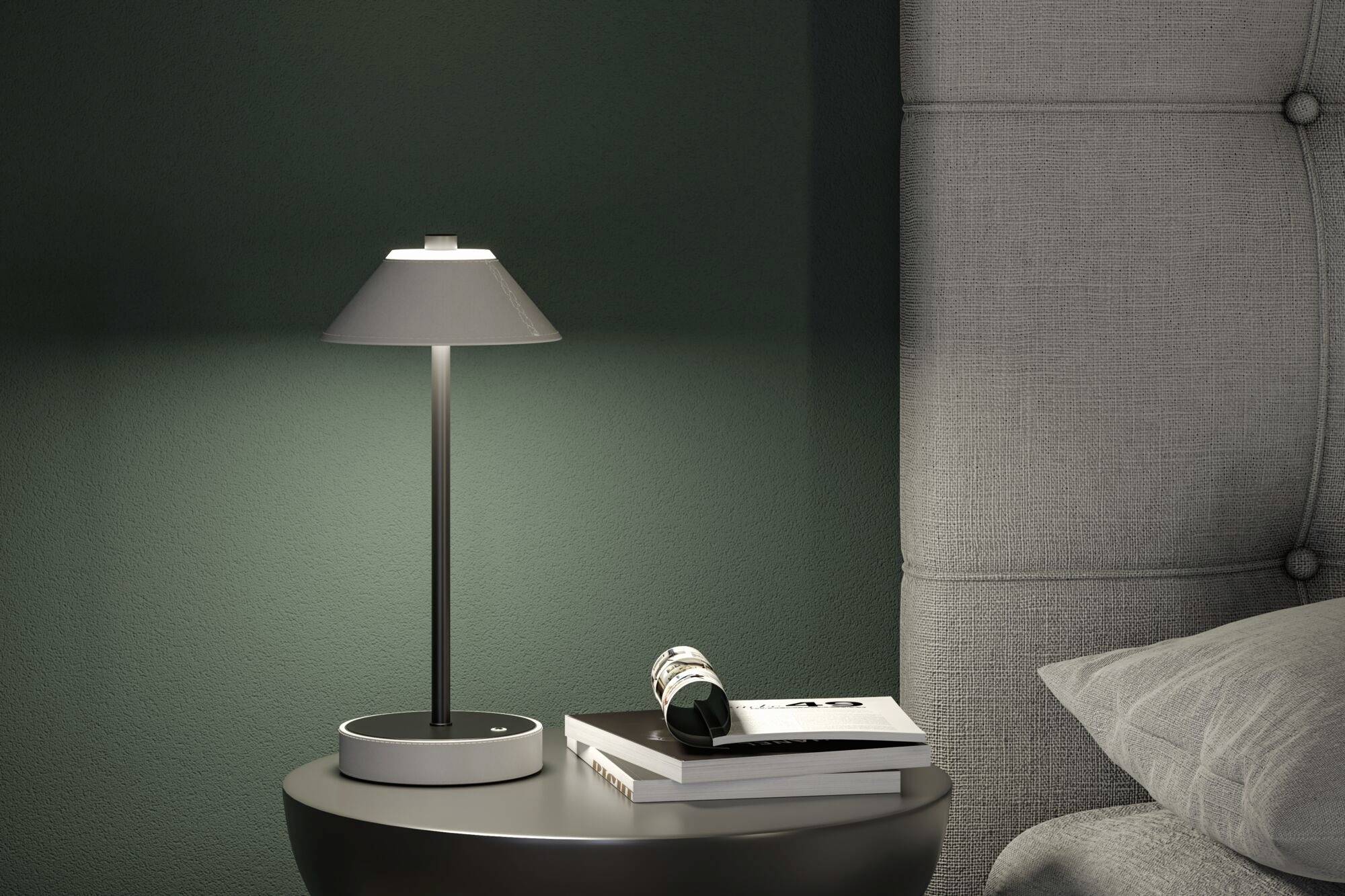 Nočná lampa svieti na okrúhlom stolíku vedľa postele. Na stolíku ležia knihy a zrolovaný časopis.