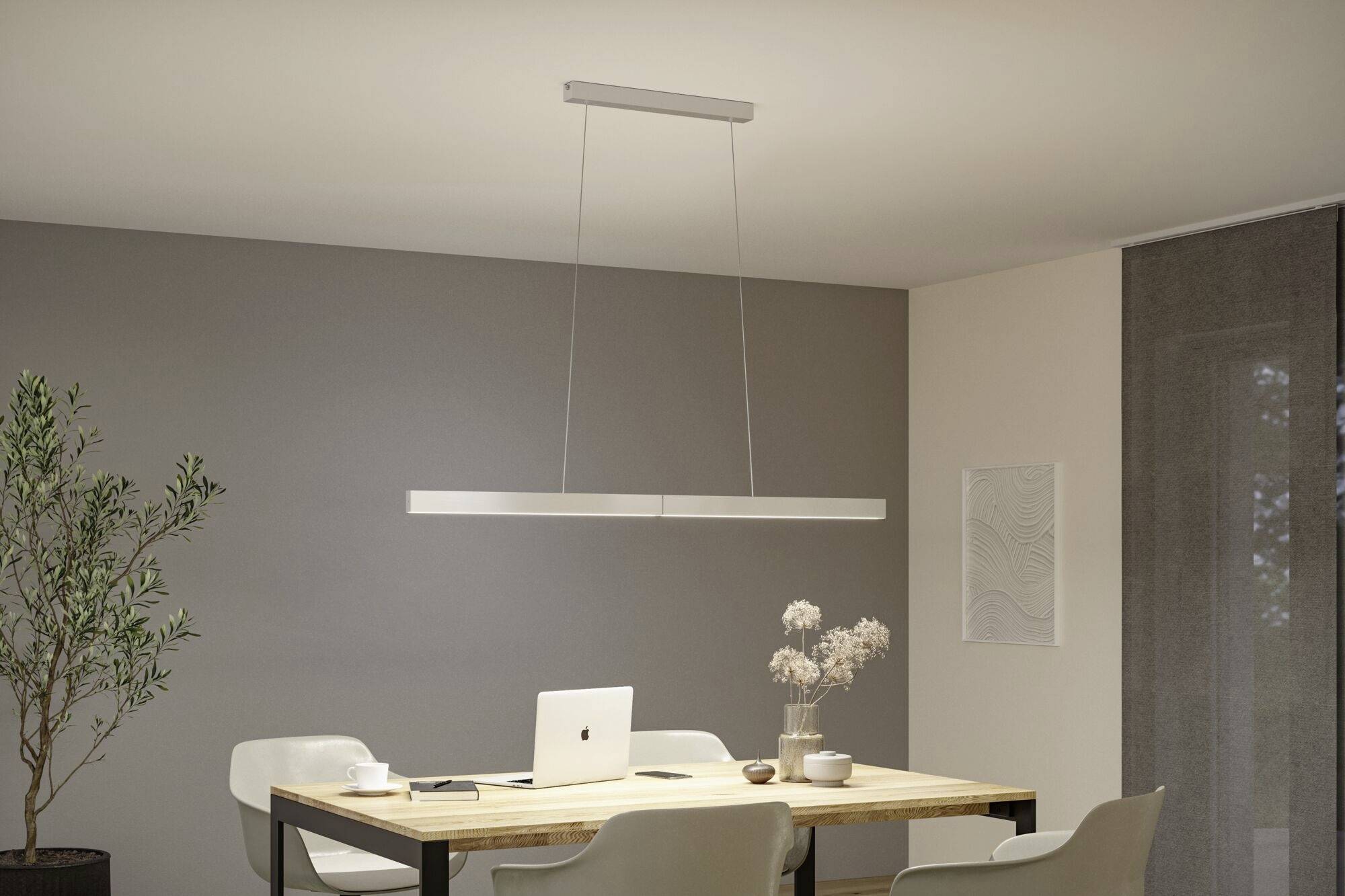 Moderná miestnosť s dreveným stolom a štyrmi stoličkami. Na stole leží laptop a dekorácie. Lineárna závesná lampa osvetľuje priestor.