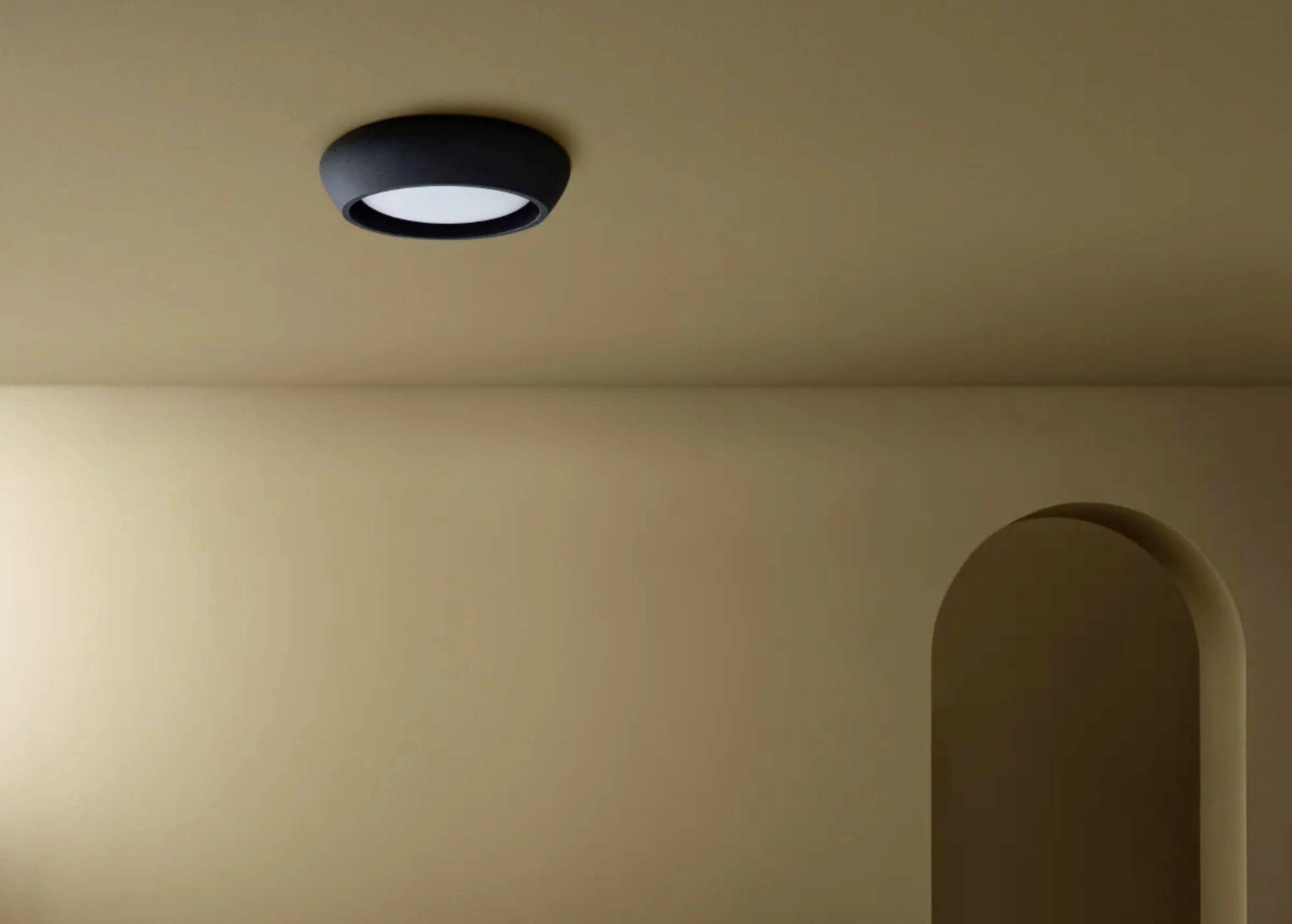 Moderná stropná lampa v minimalistickom priestore s oblúkovitým otvorom na pravej stene, béžové steny.