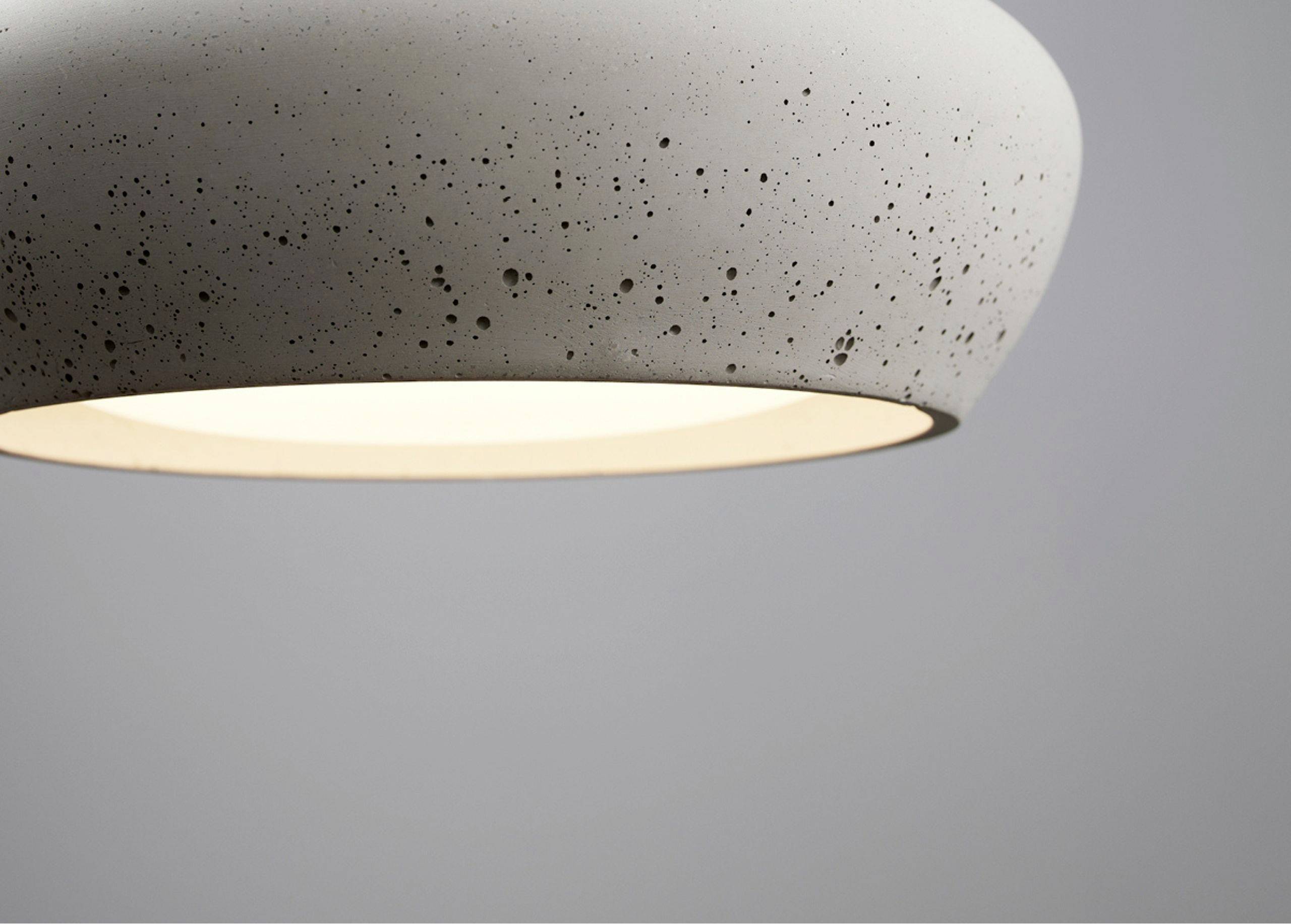 Biela, moderne závesné svietidlo s škvrnkatou textúrou, ktoré svieti do sivého pozadia.