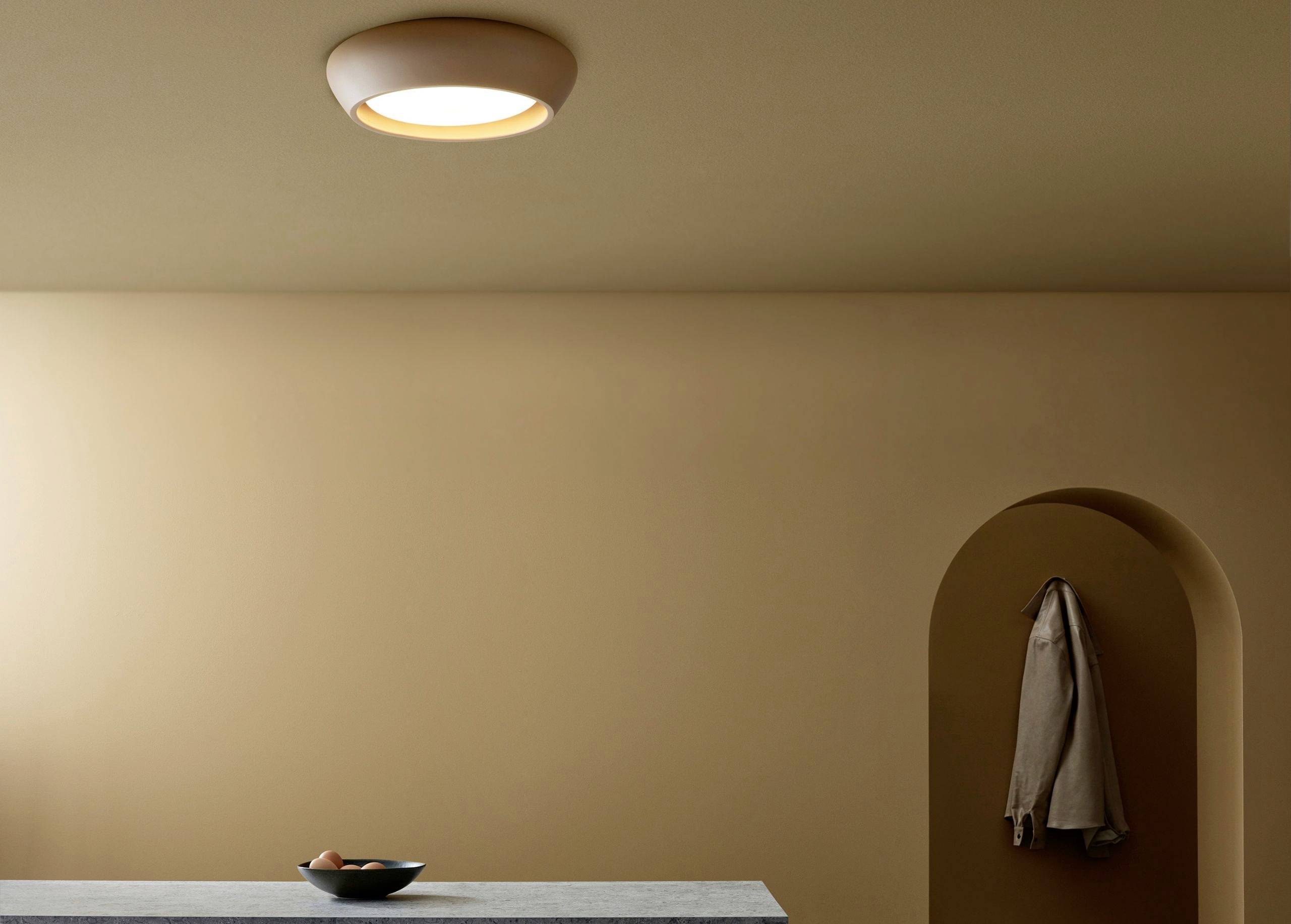 Svetlá, minimalistická izba s krémovými stenami; miska s ovocím stojí na stole, kabát visí na háčiku na stene.