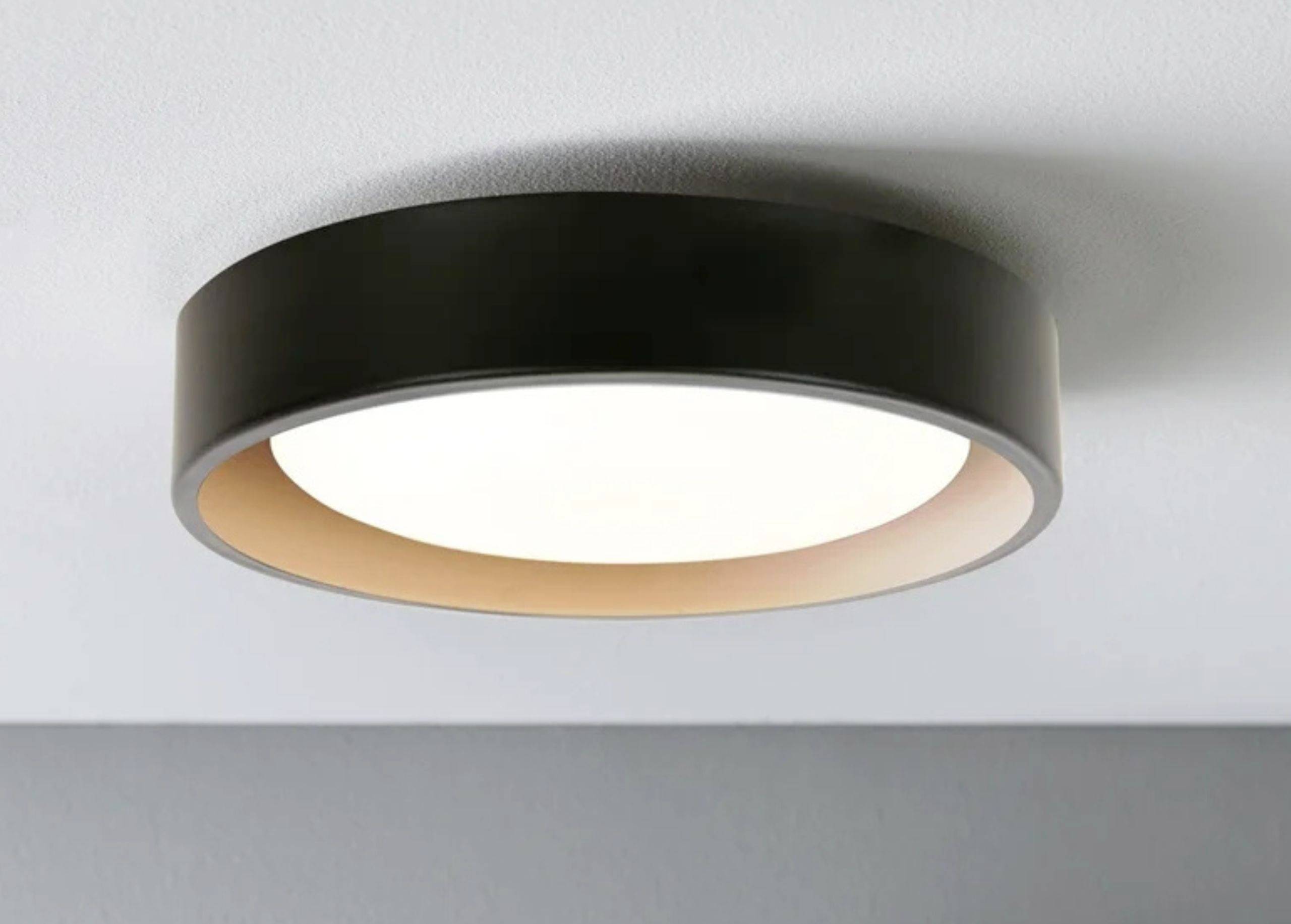 Okrúhle stropné svietidlo čiernej farby s teplým bielym svetlom, namontované na bielom strope.