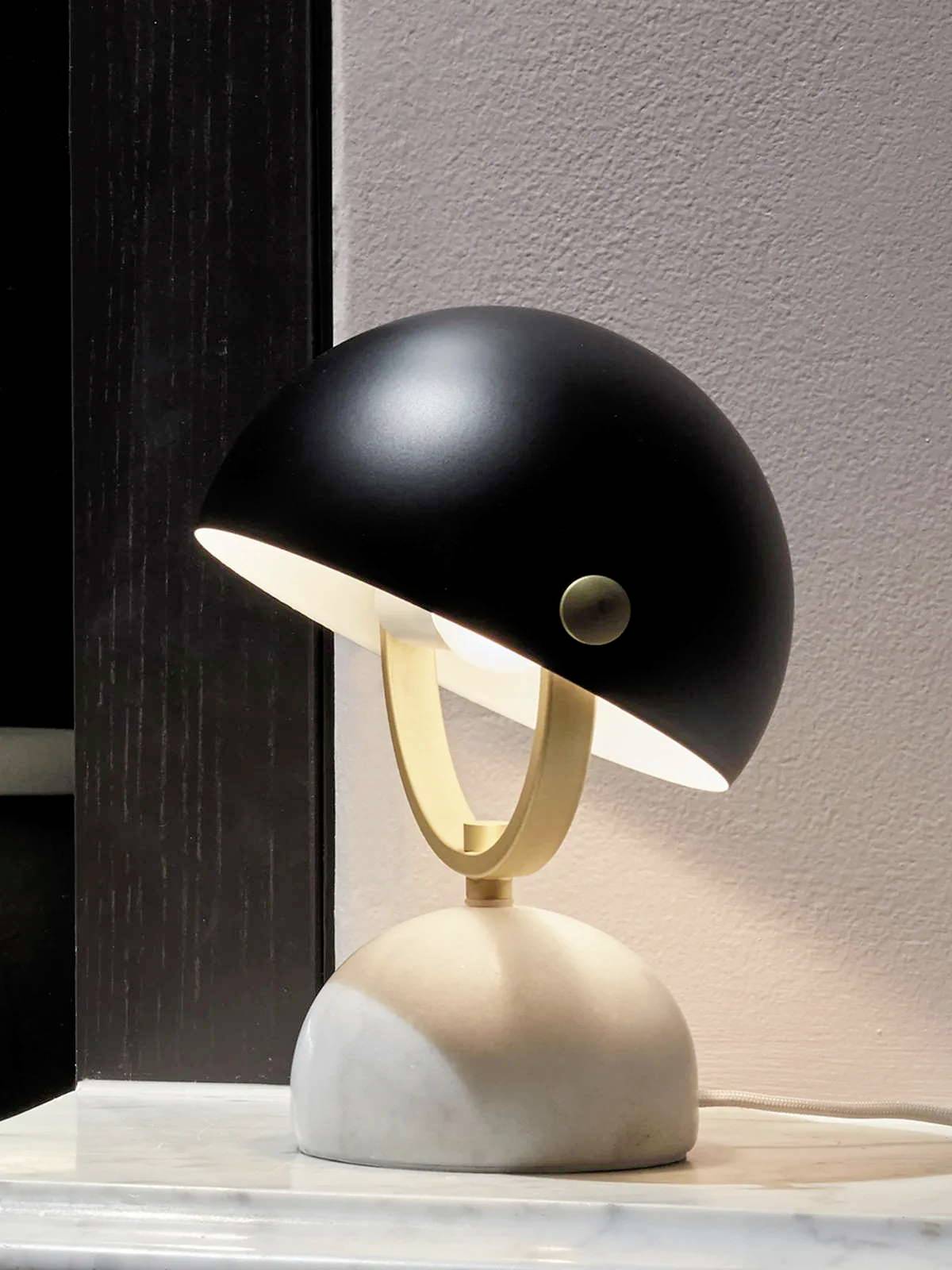 Moderná stolná lampa s čiernym tienidlom a mramorovanou základňou jemne osvetľuje priestor, pričom stojí na stole.