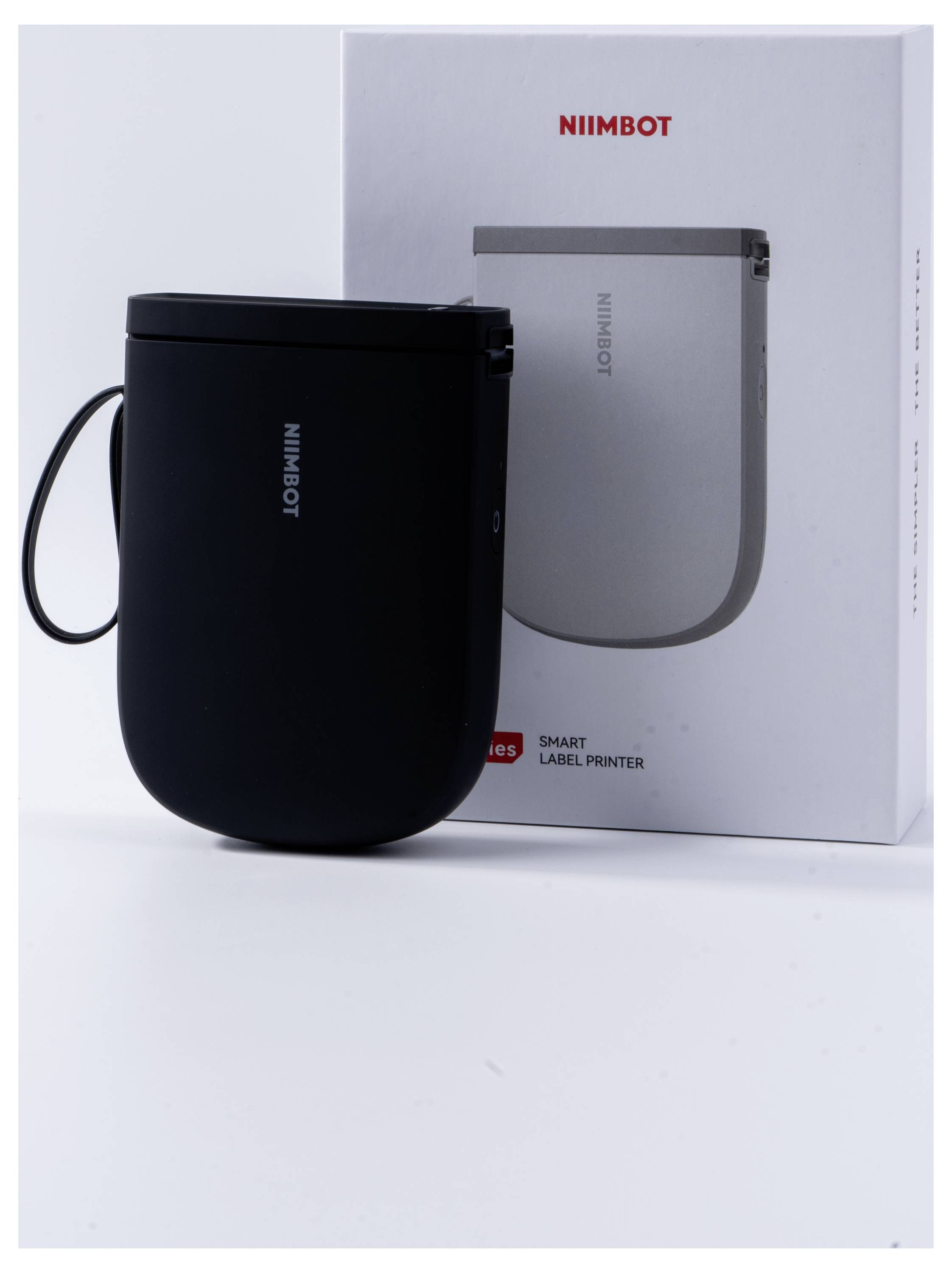 Čierny tlačiareň štítkov od NIIMBOT stojí pred svojím obalom. Na obale je napísané 'NIIMBOT Smart Label Printer'.