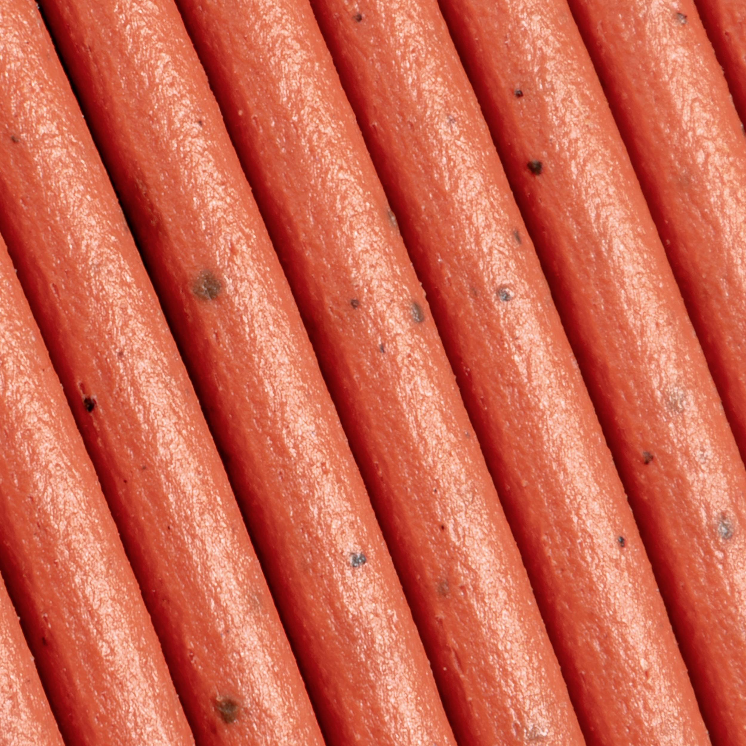Detailný záber hladkých, oranžových káblov, ktoré vedú paralelne vedľa seba. Povrch vykazuje malé tmavé škvrny.