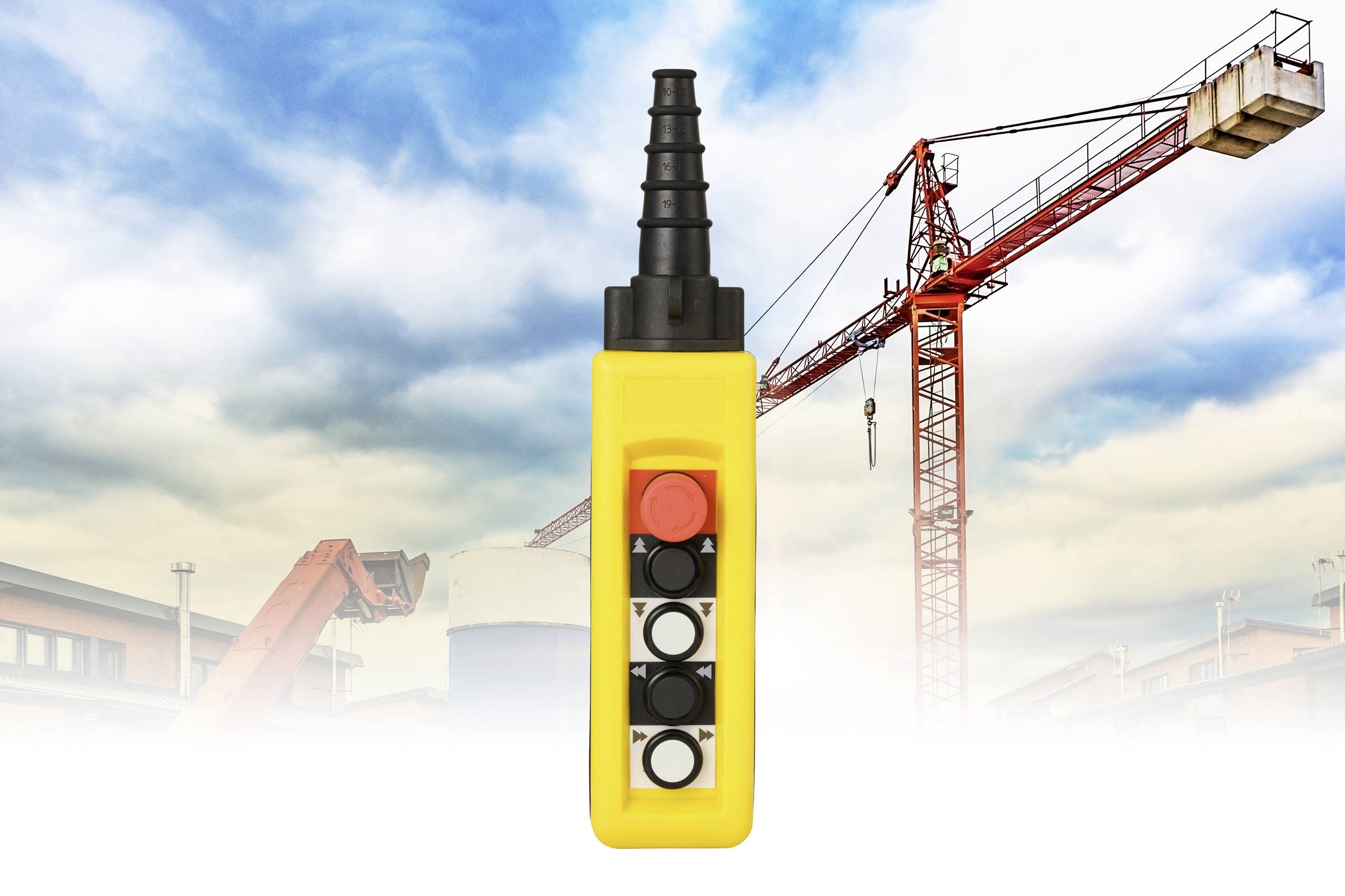 Žltý priemyselný diaľkový ovládač s tlačidlami, umiestnený pred pozadím staveniskových žeriavov a budov pod modrým nebom.