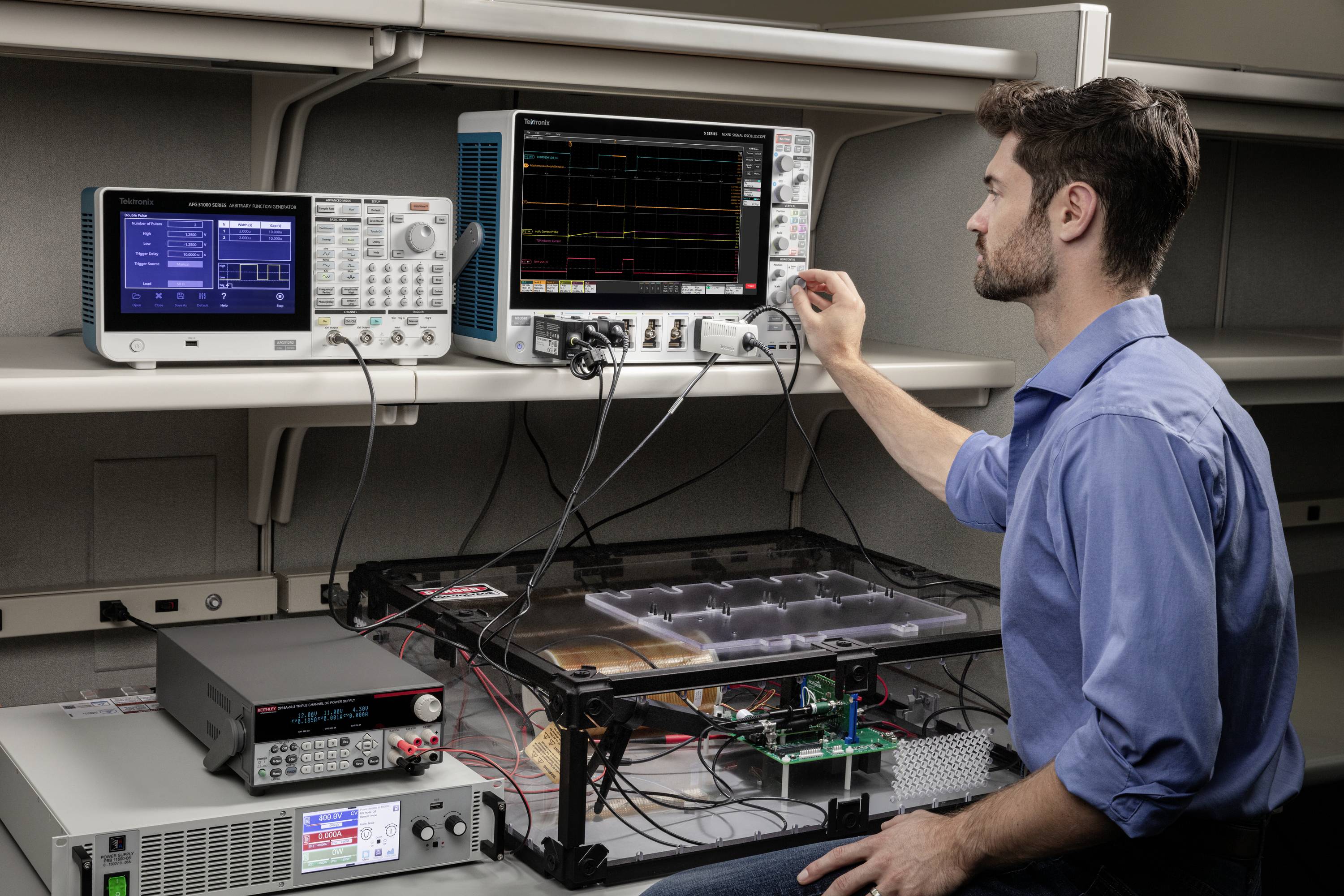 Muž pracuje na osciloskope v laboratóriu. Rôzne elektronické zariadenia sú usporiadané na stole. Sústreďuje sa na merania.