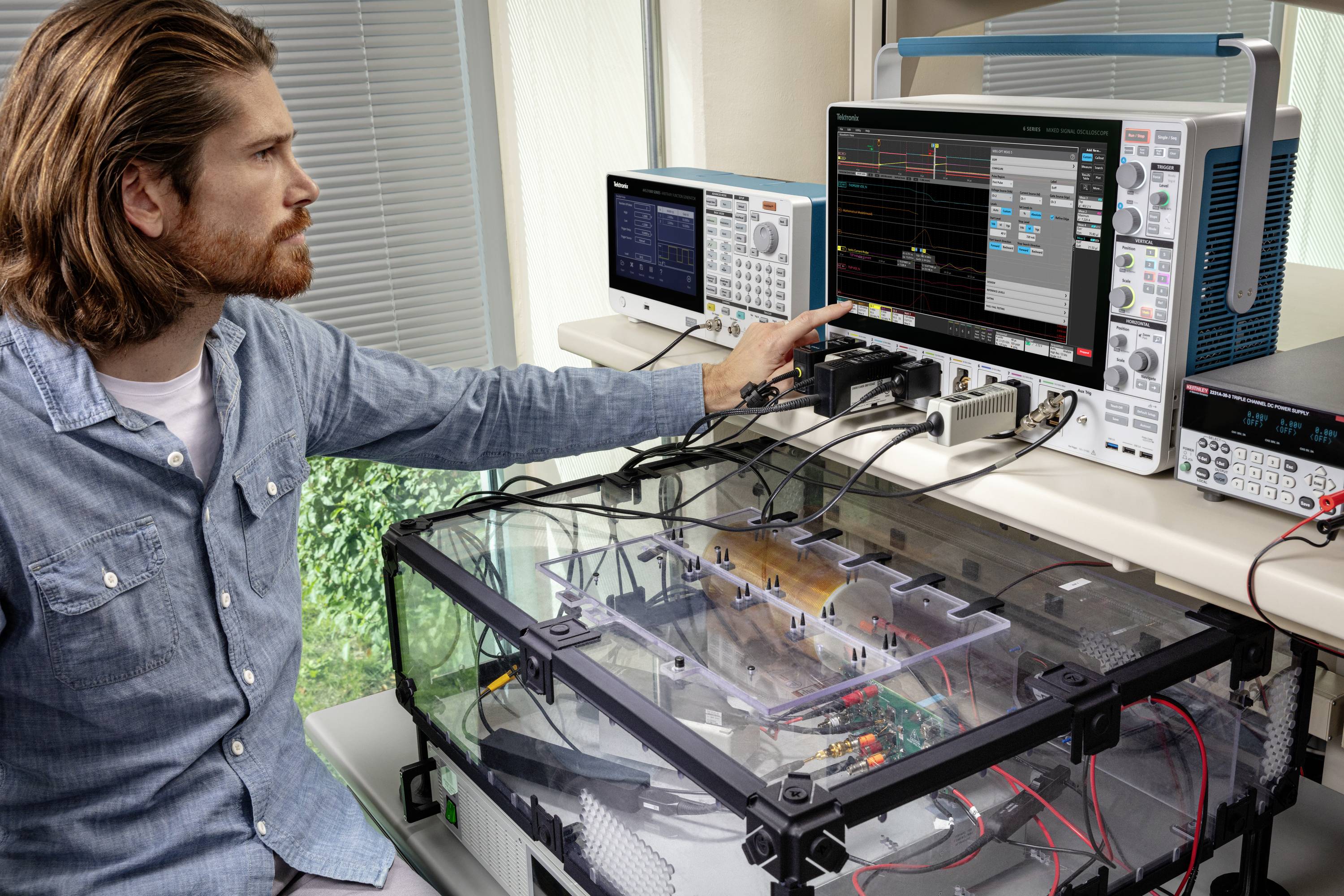 Muž v laboratóriu obsluhuje elektronické meracie prístroje s osciloskopom. Analyzuje dáta na obrazovke, sústredene a pozorne.