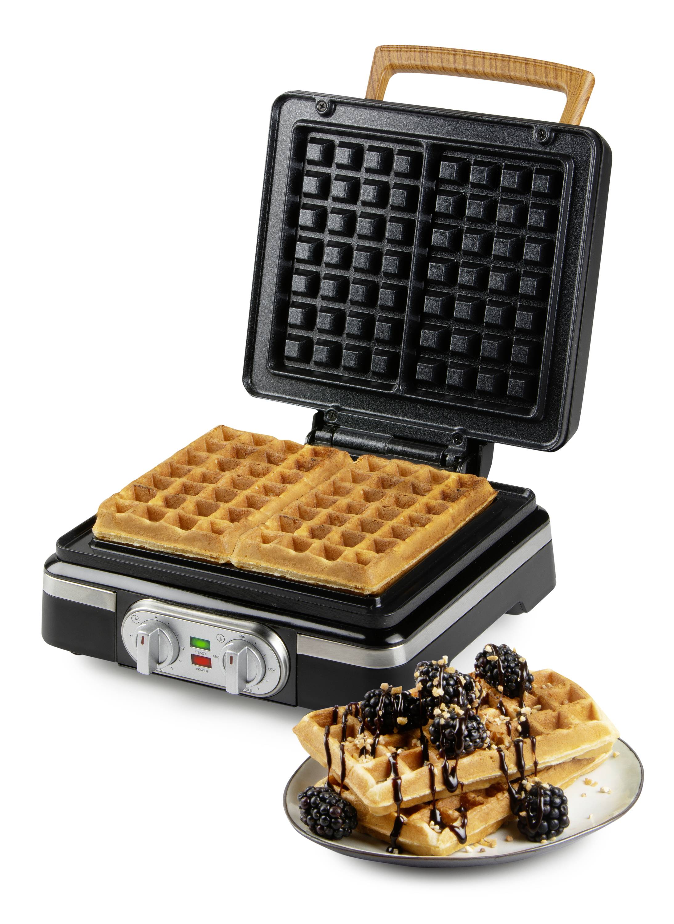 Elektrická wafliovač s dvomi upečenými wafľami; vedľa tanier s hotovými servírovanými wafľami, zdobenými čokoládovou omáčkou a ovocím.