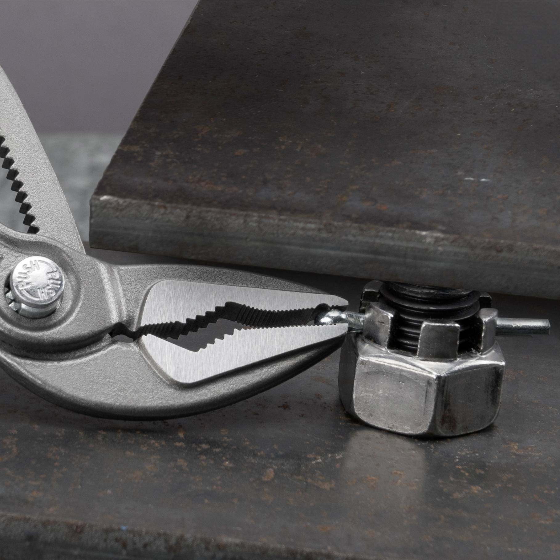 Kliešte držia skrutkovú maticu. Leží na kovovom povrchu vedľa ďalšieho oceľového uholníka.