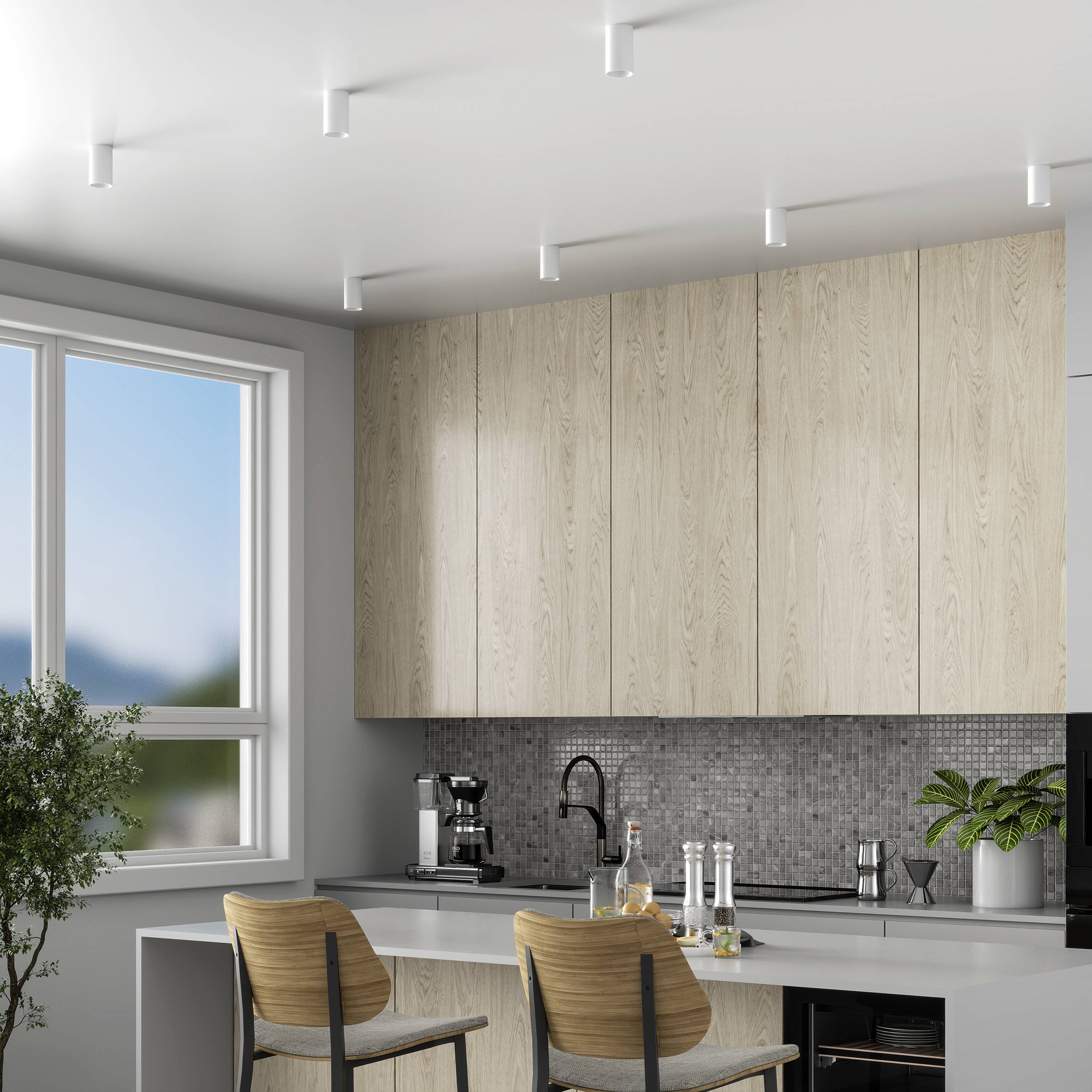 Moderná kuchyňa s veľkou presklenou stenou, drevenými skrinkami, sivými dlaždicami a dvomi barových stoličkami. Svetlá a minimalisticky zariadená.