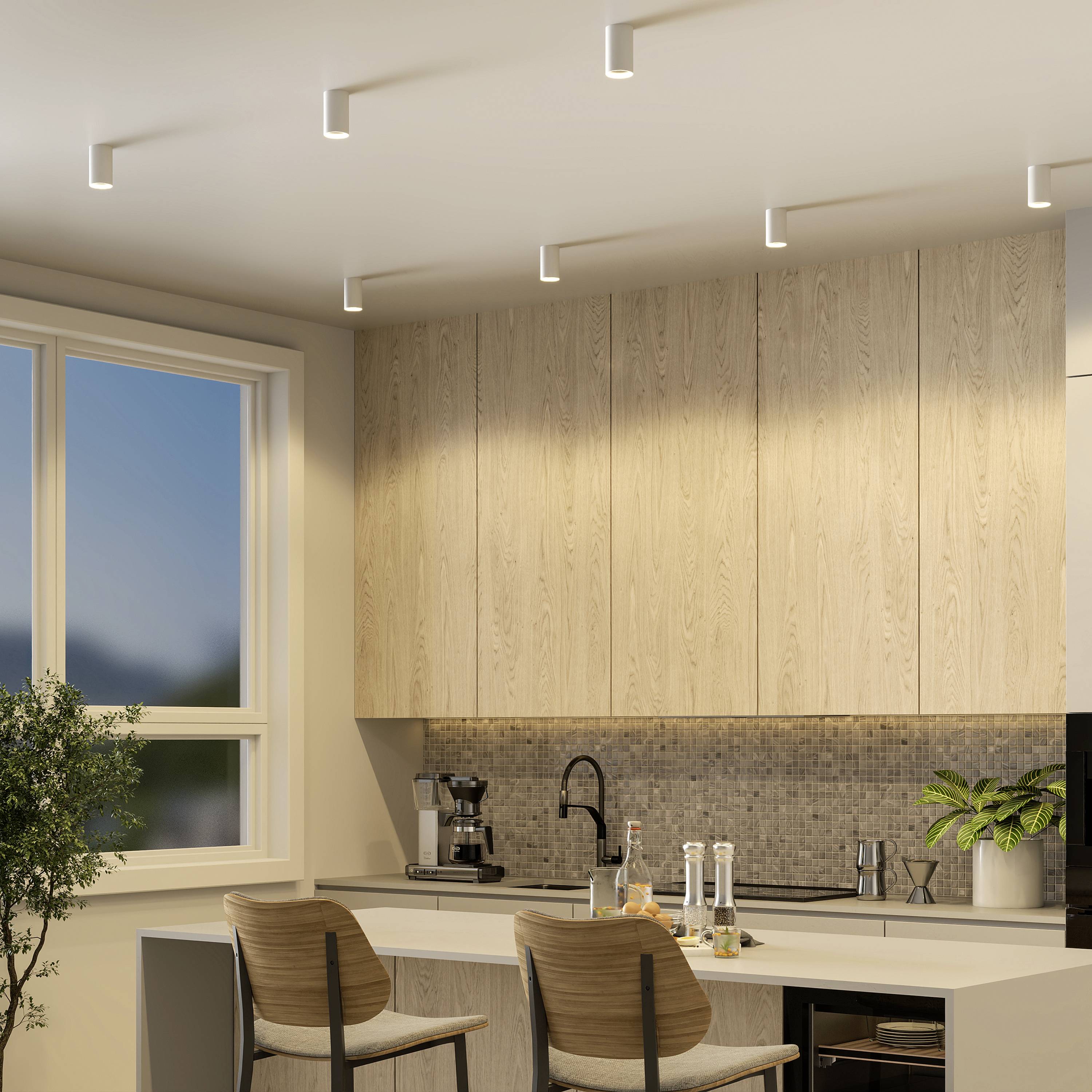 Moderná kuchyňa so svetlými drevenými skrinkami, veľkým výhľadom z okna, barovou stoličkou a stolom s korením a rastlinami.