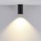 Čierna stropná lampa vyžaruje teplé svetlo na bielu stenu. Minimalistický dizajn so zameraním na svetelný efekt.