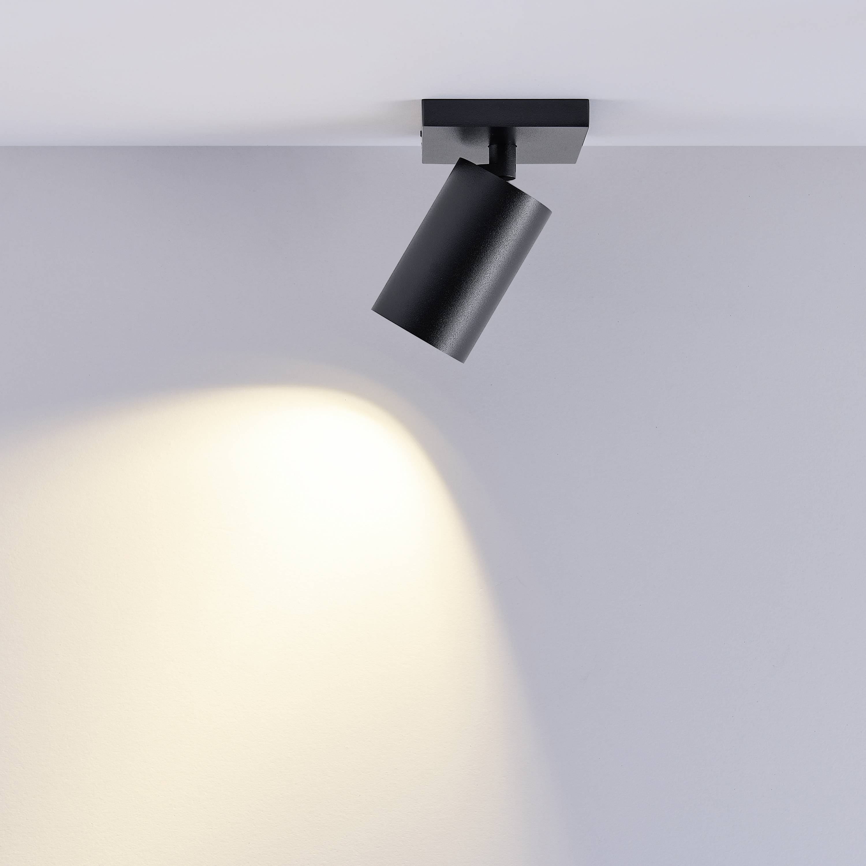 Čierno-sivý stropný reflektor jasne osvecuje stenu a vytvára fokusovaný svetelný kužeľ. Moderný osvetľovací prvok v interiéri.