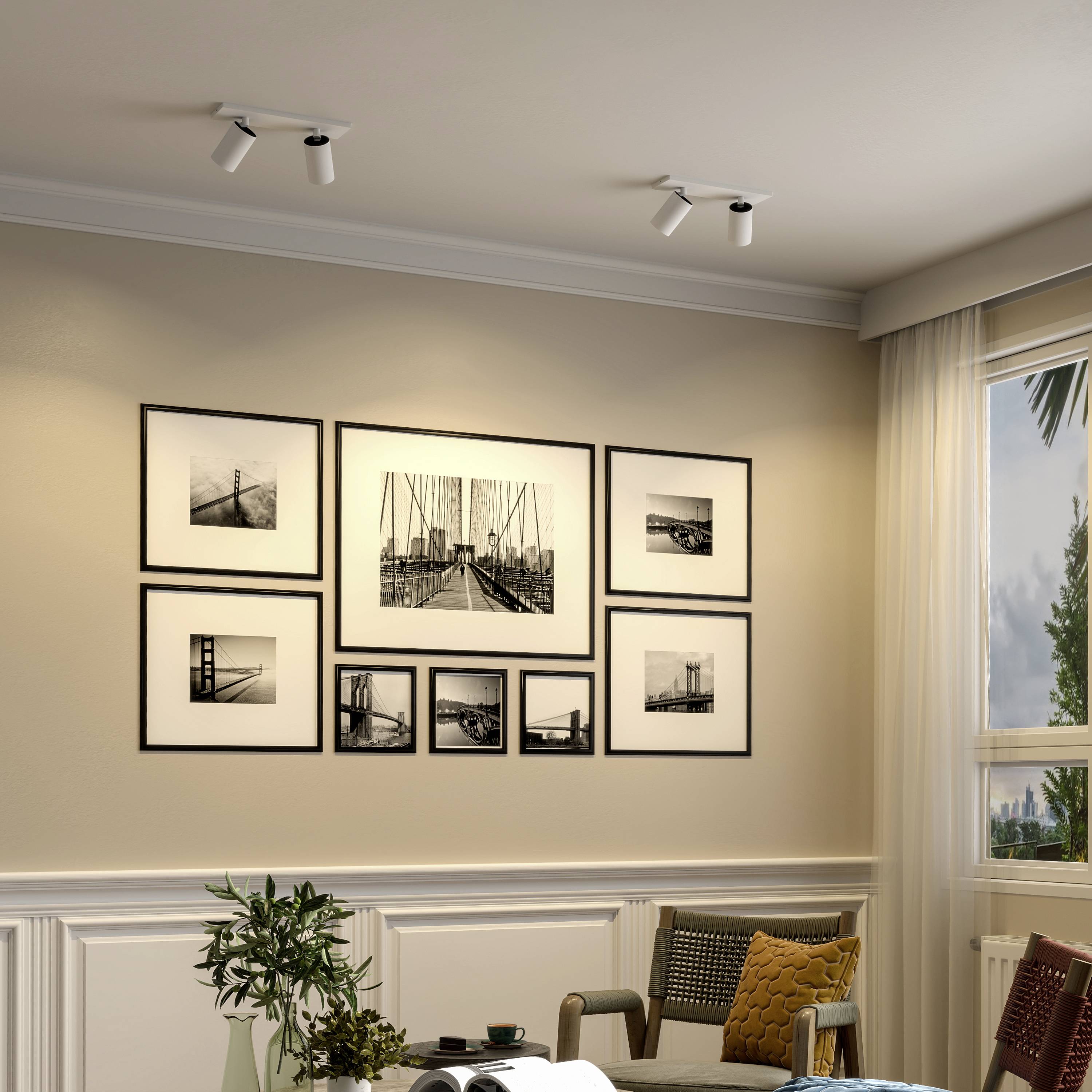 Obývacia izba s viacerými zarámovanými čiernobielymi fotografiami na stene, modernými reflektormi, béžovou sedačkou a výhľadom z okna.