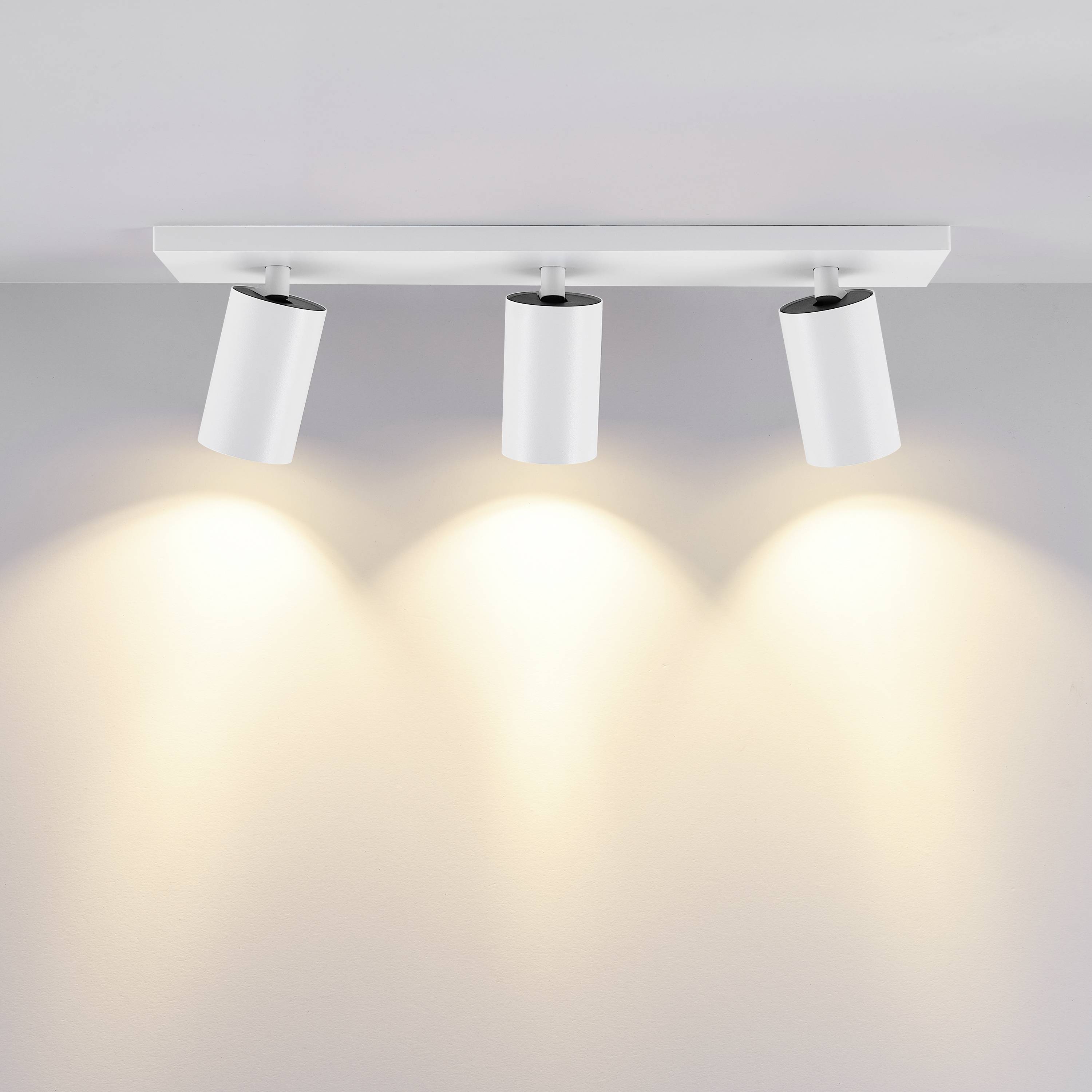 Biela stropná lampa s tromi nastaviteľnými bodovými svetlami, ktoré premietajú teplé svetlo na stenu. Ideálna pre moderné obytné priestory.