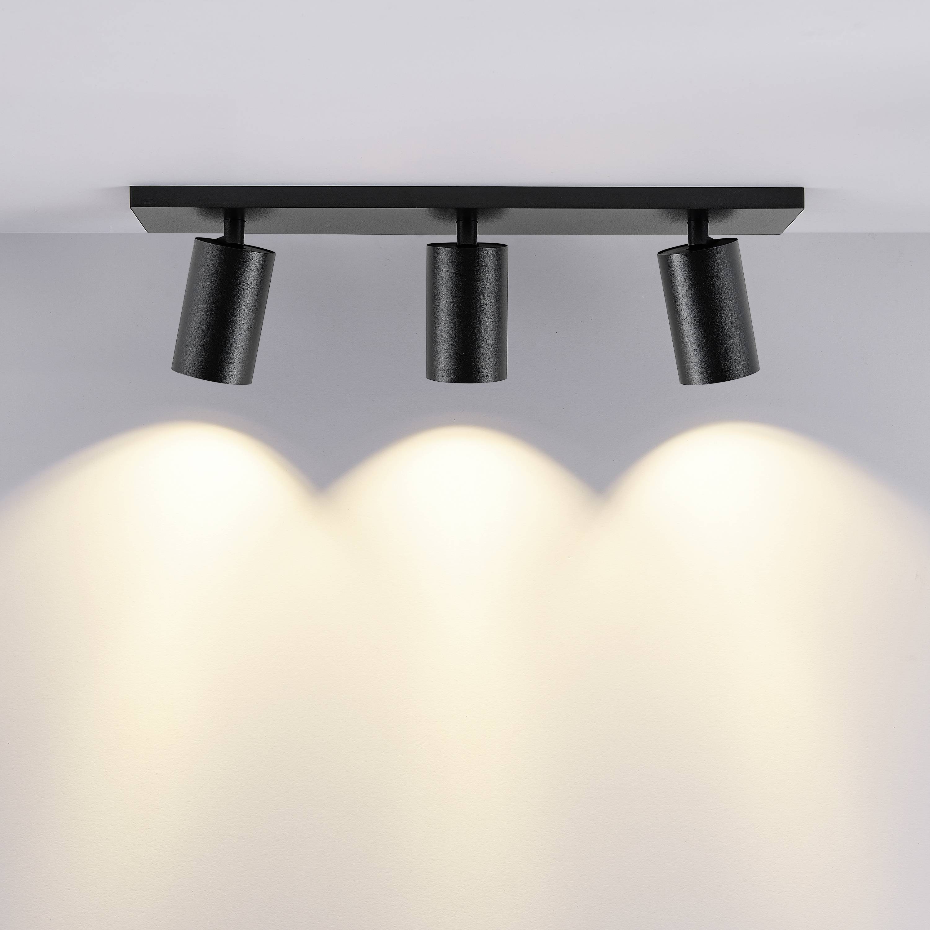Tri čierne stropné reflektory jasne svietia smerom nadol a vytvárajú rovnomerné osvetlenie v modernej miestnosti.