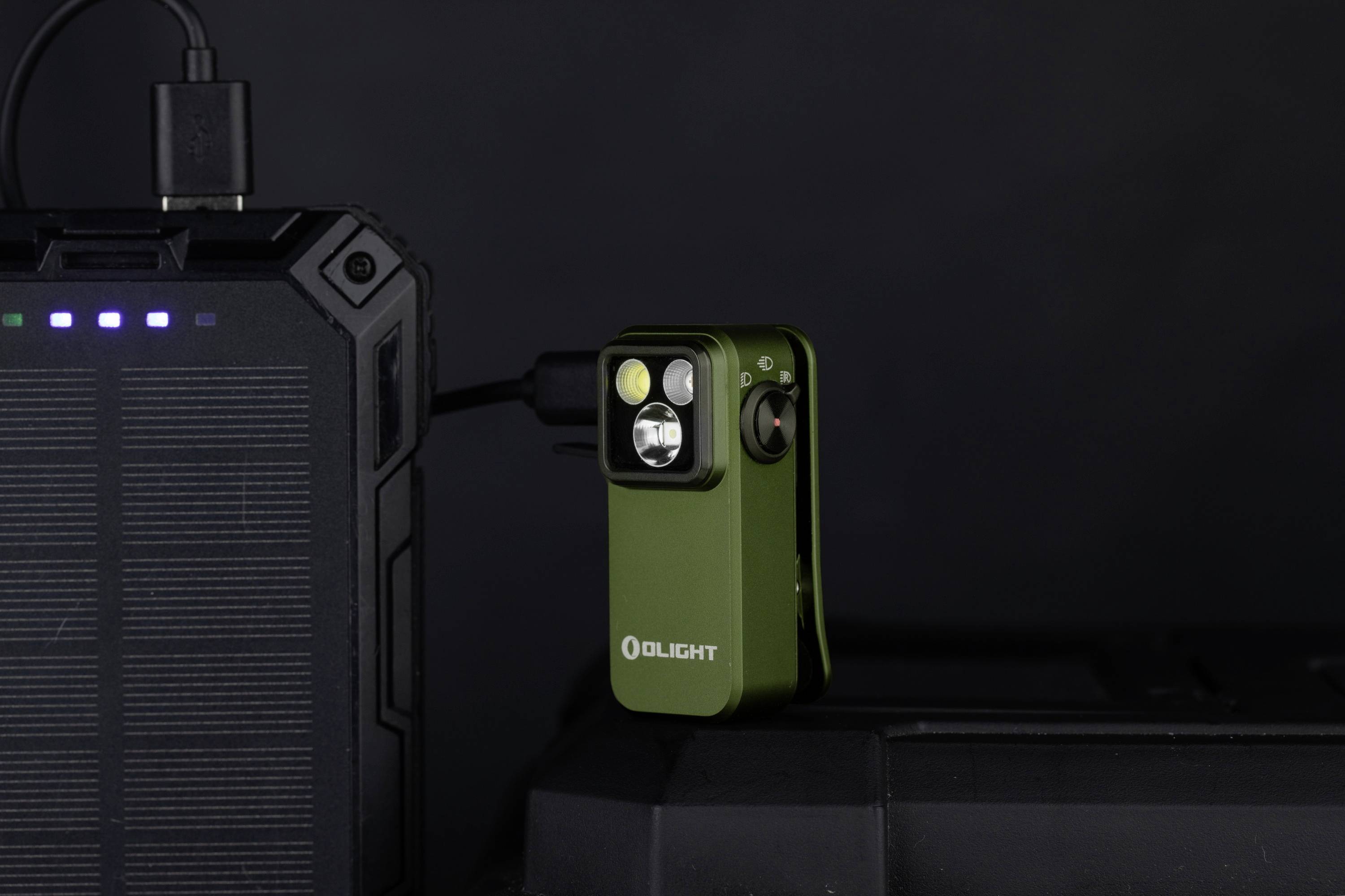 Zelená vrecková LED baterka Olight na tmavom pozadí, pripojená k nabíjačke.