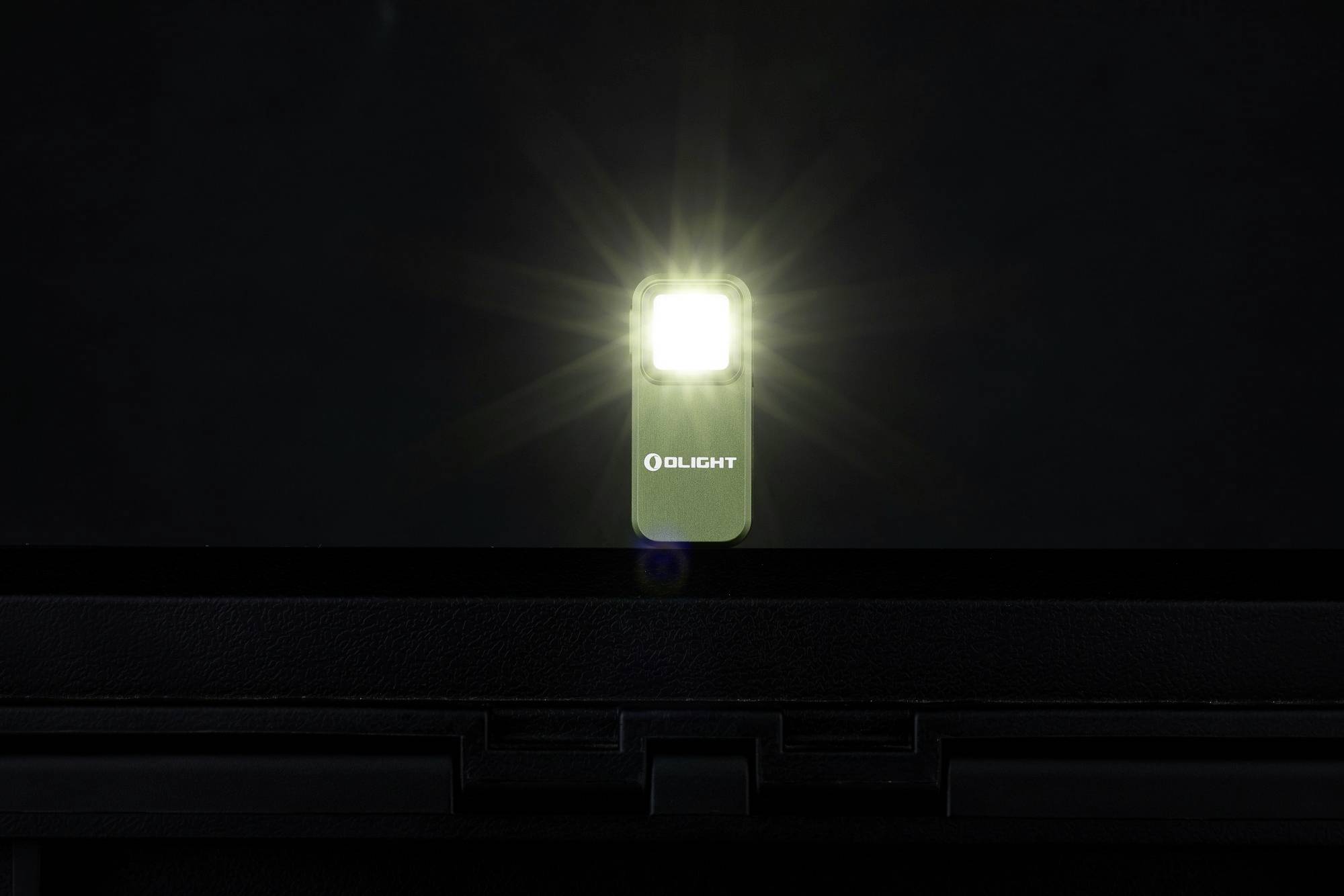 Svietiaca baterka pred tmavým pozadím, svetlo vyžarujúce z lampy, značka 'Olight' viditeľná na prednej strane.