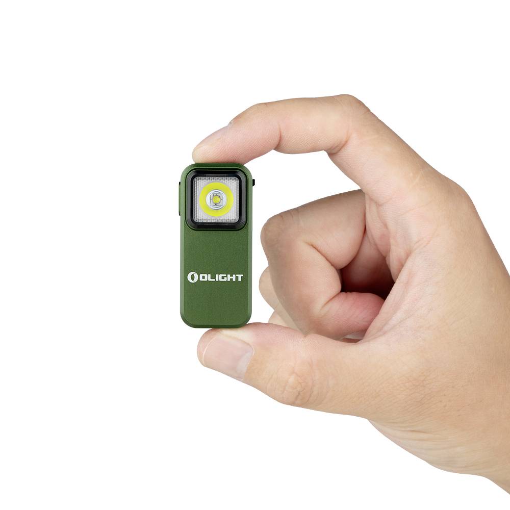Ruka drží malú zelenú LED baterku značky Olight. Baterka má štvorcový svetelný panel.