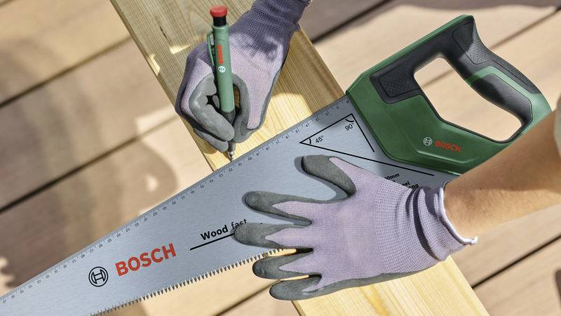 Dve ruky v rukaviciach kreslia perom na drevo, pričom držia ručnú pílu Bosch priloženú k doske.