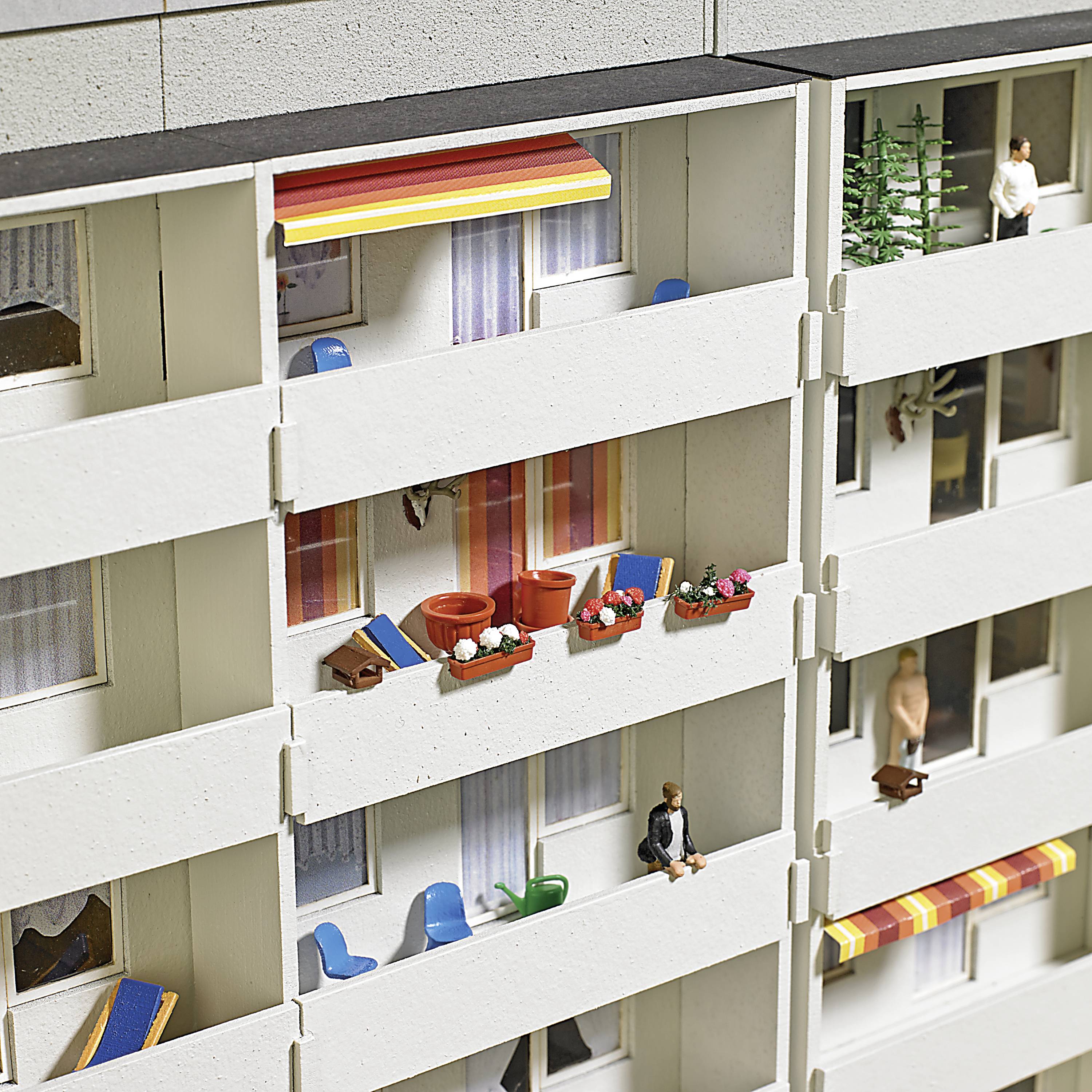 Biela architektonická maketa budovy s balkónmi; niektoré s farebnými markízami, rastlinami a nábytkom. Na jednom balkóne sedí miniatúrna figúrka.