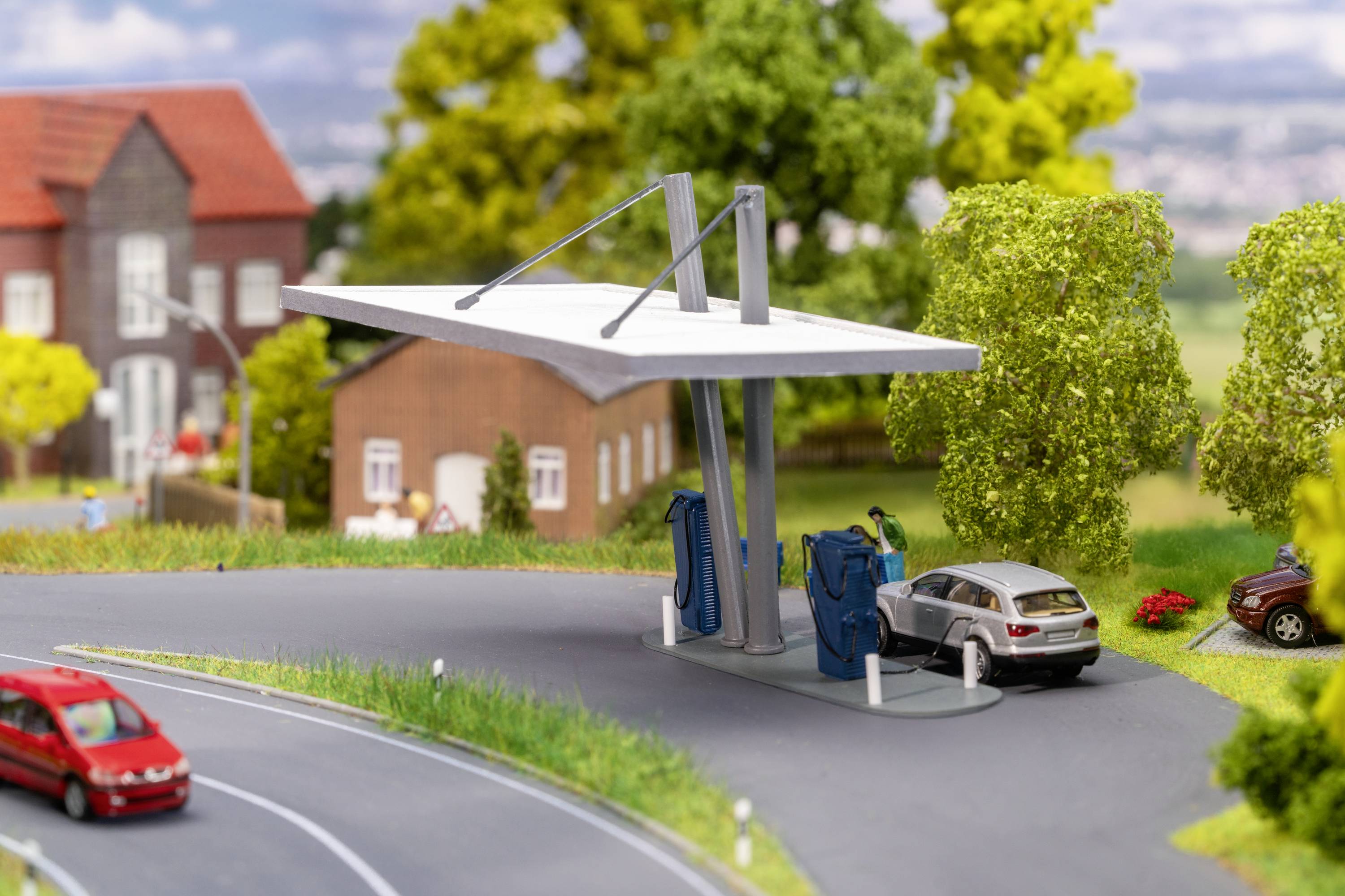 Elektromobil sa nabíja na nabíjacej stanici vo vidieckom prostredí. V pozadí sú viditeľné domy a stromy.