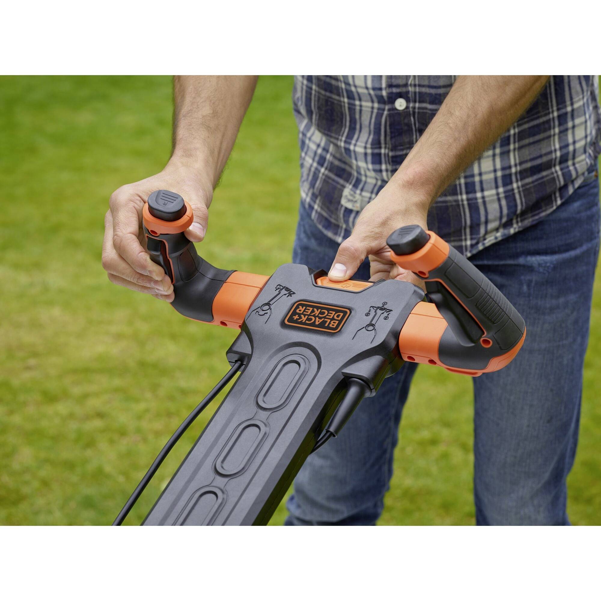 Osoba drží rukoväť elektrického kosačky na zelenej tráve. Kosačka je čierna s oranžovými akcentmi.
