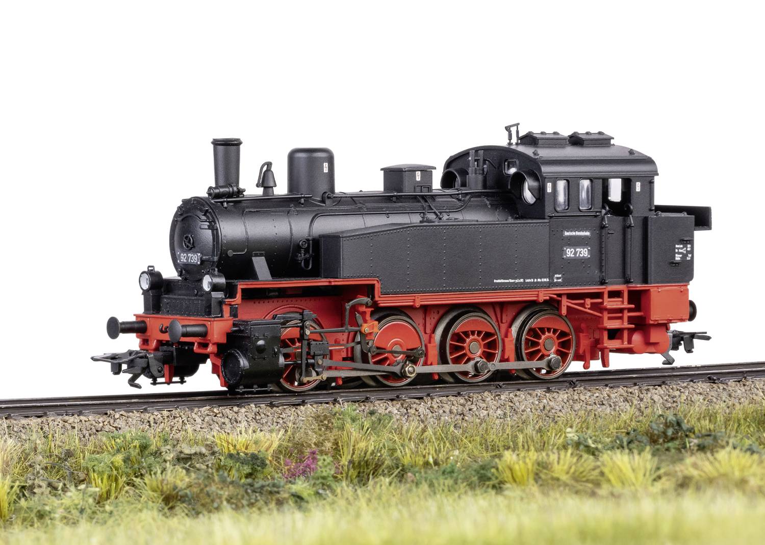 Čierna parná lokomotíva s červeným podvozkom stojí na železničných koľajach v lúčnej krajine, model 130.7716.