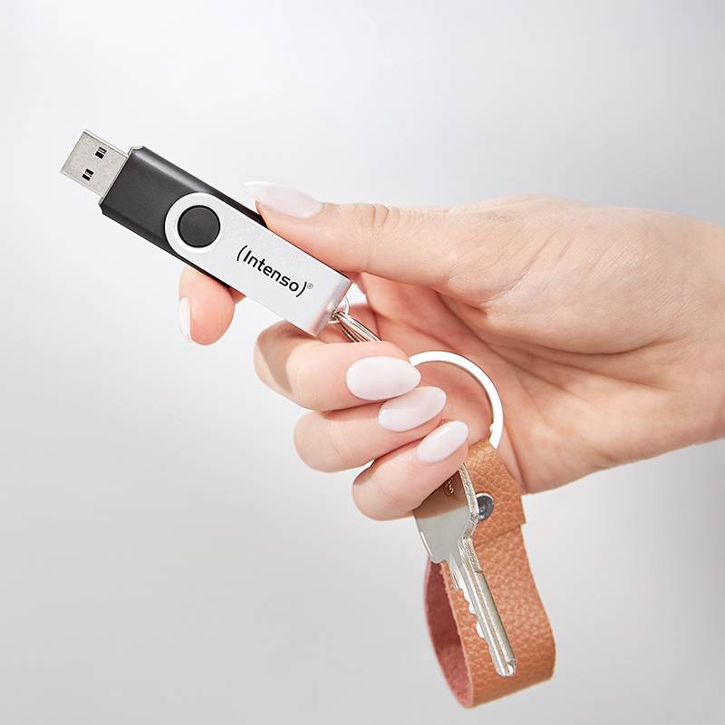 Ruka drží USB flash disk označený ako 'Intenso' a hnedý kožený prívesok na kľúče s kľúčom, čo symbolizuje prenosnú dátovú úložisko a prístup.