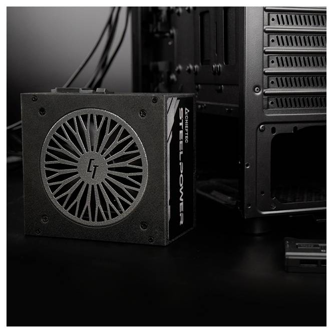 Počítačový napájací zdroj označený SteelPower vedľa PC skrine, prezentujúci čierny dizajn a viditeľnú mriežku ventilátora.