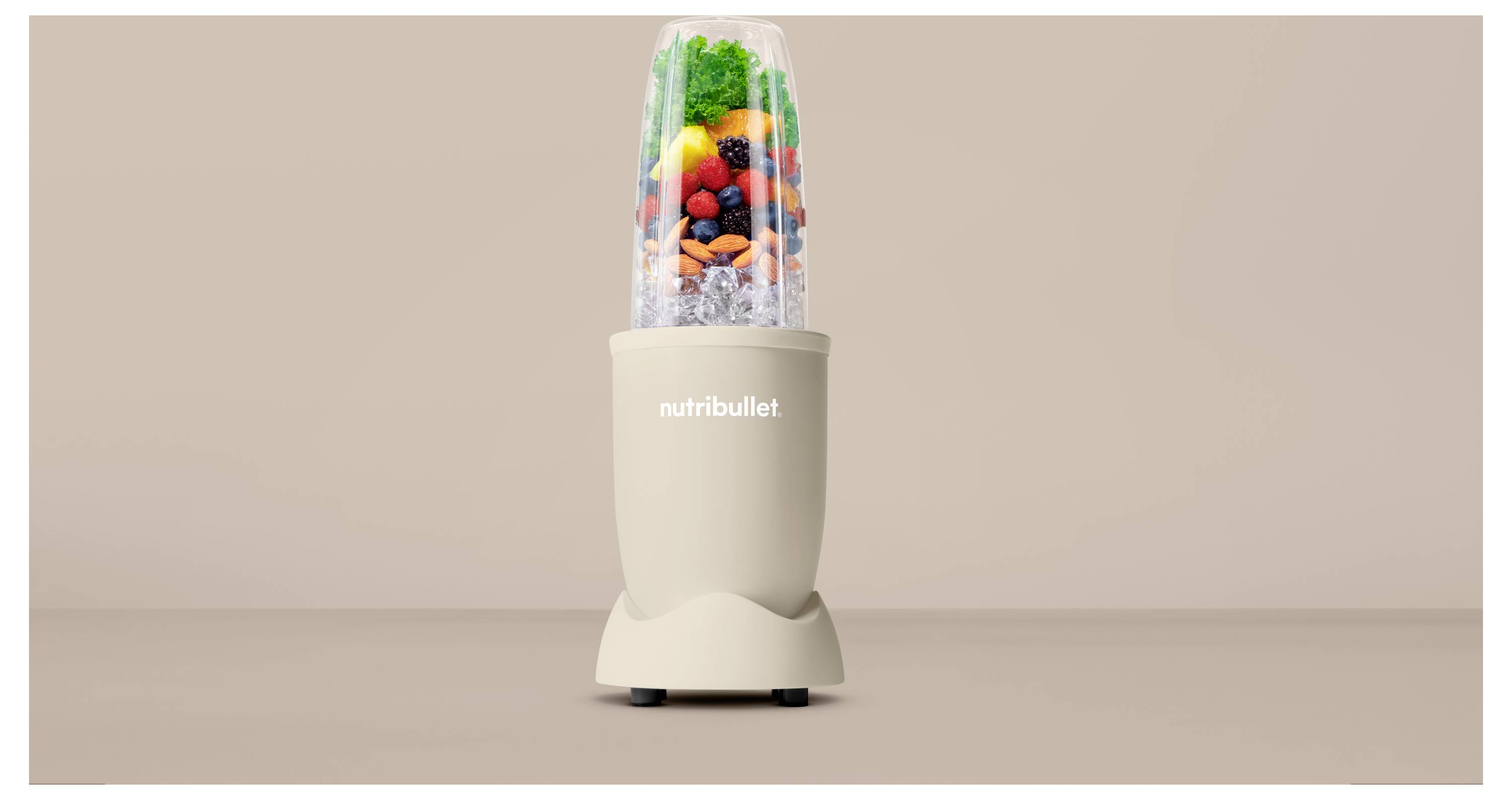 Béžový mixér Nutribullet naplnený rôznorodým farebným ovocím a zeleninou, umiestnený pred neutrálnym pozadím.