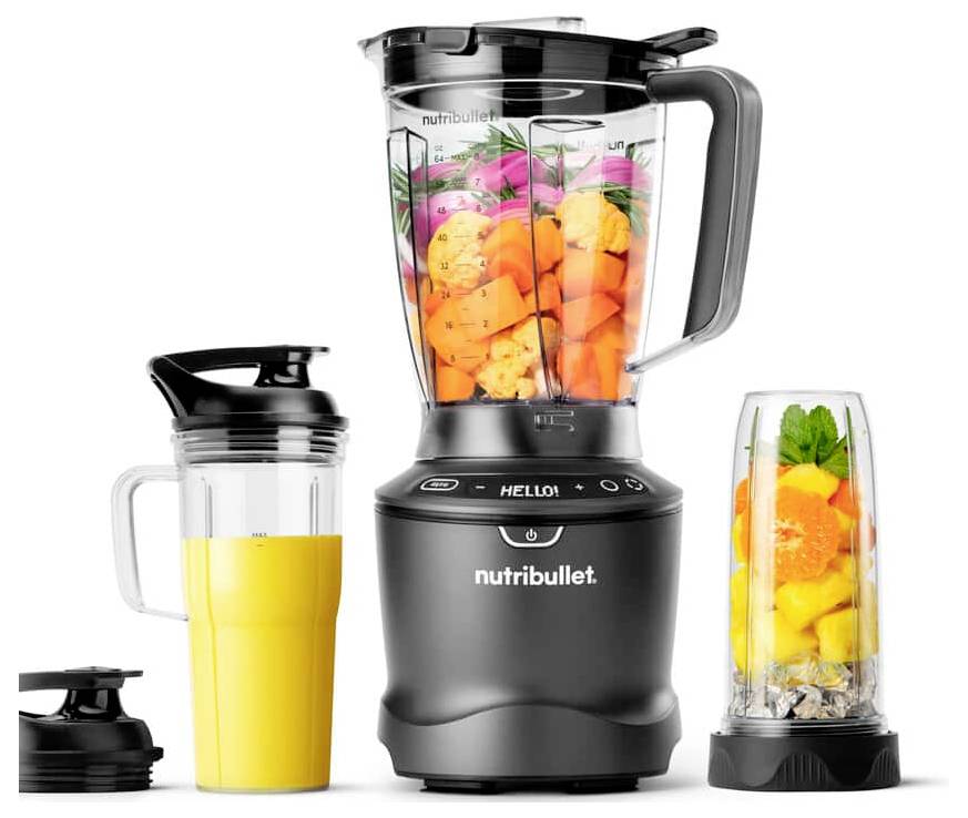 Čierny mixér Nutribullet s kanvicami naplnenými farebnými ovocím a šálkou pomarančového smoothie vedľa neho.