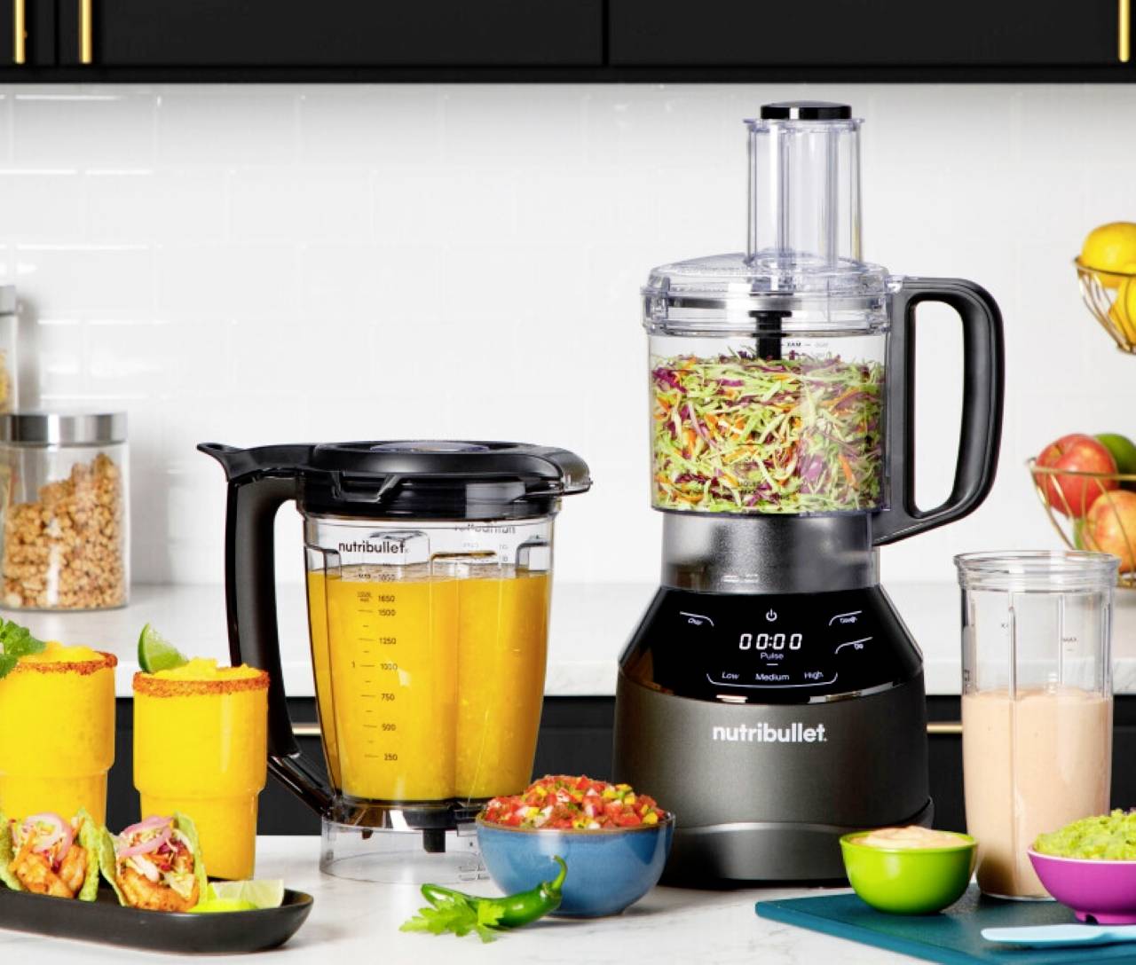 Mixér a kuchynský robot na kuchynskej doske s nakrájanou zeleninou, ovocím a smoothie vedľa nich, ktoré poukazujú na prípravu jedla.