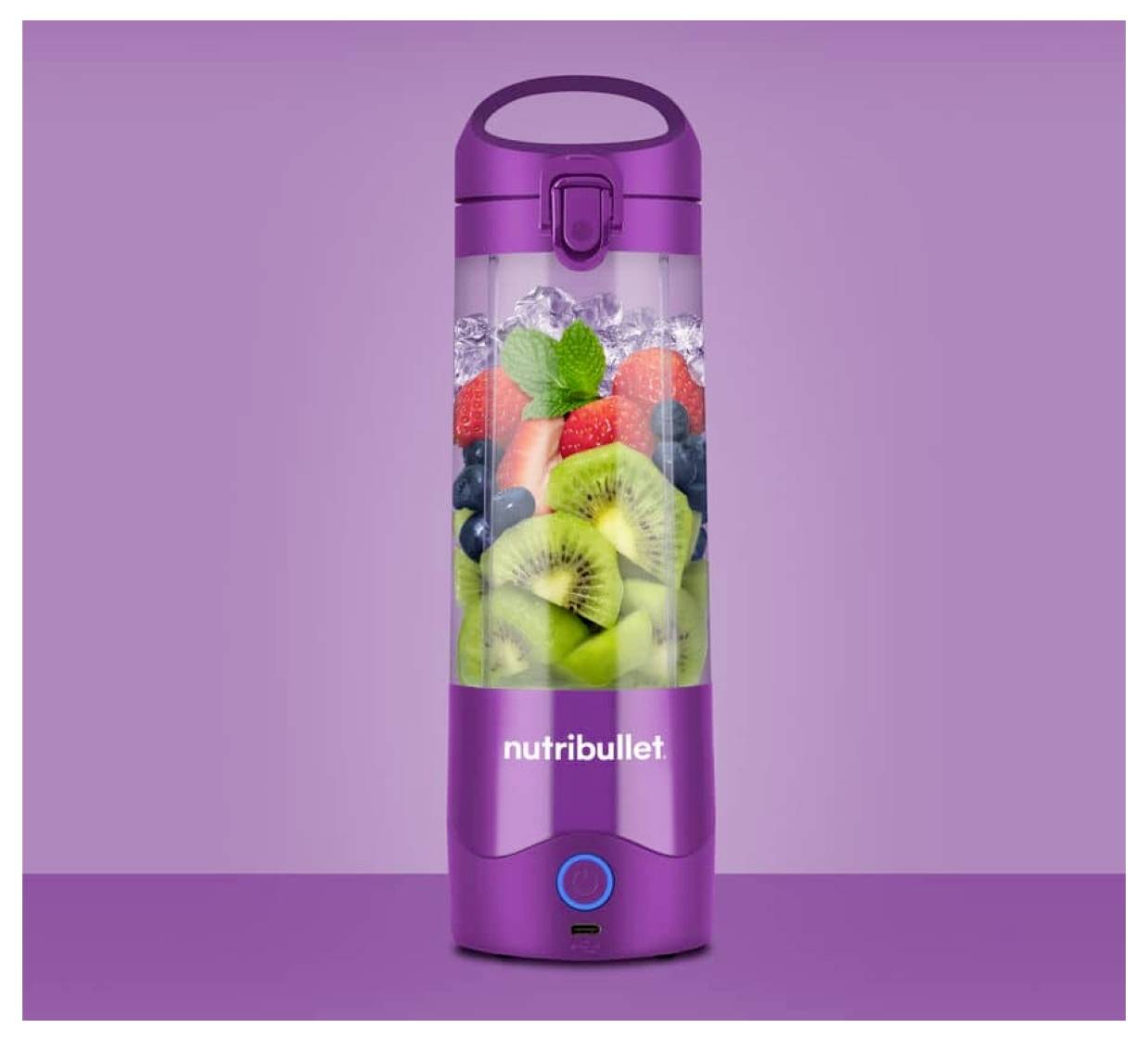 Fialová fľaša na smoothie Nutribullet naplnená ľadom, plátkami kiwi, čučoriedkami, jahodami a lístkami mäty na fialovom pozadí.