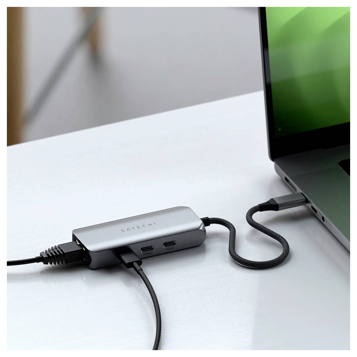 Notebook pripojený k multiportovému adaptéru s niekoľkými káblami na stole.