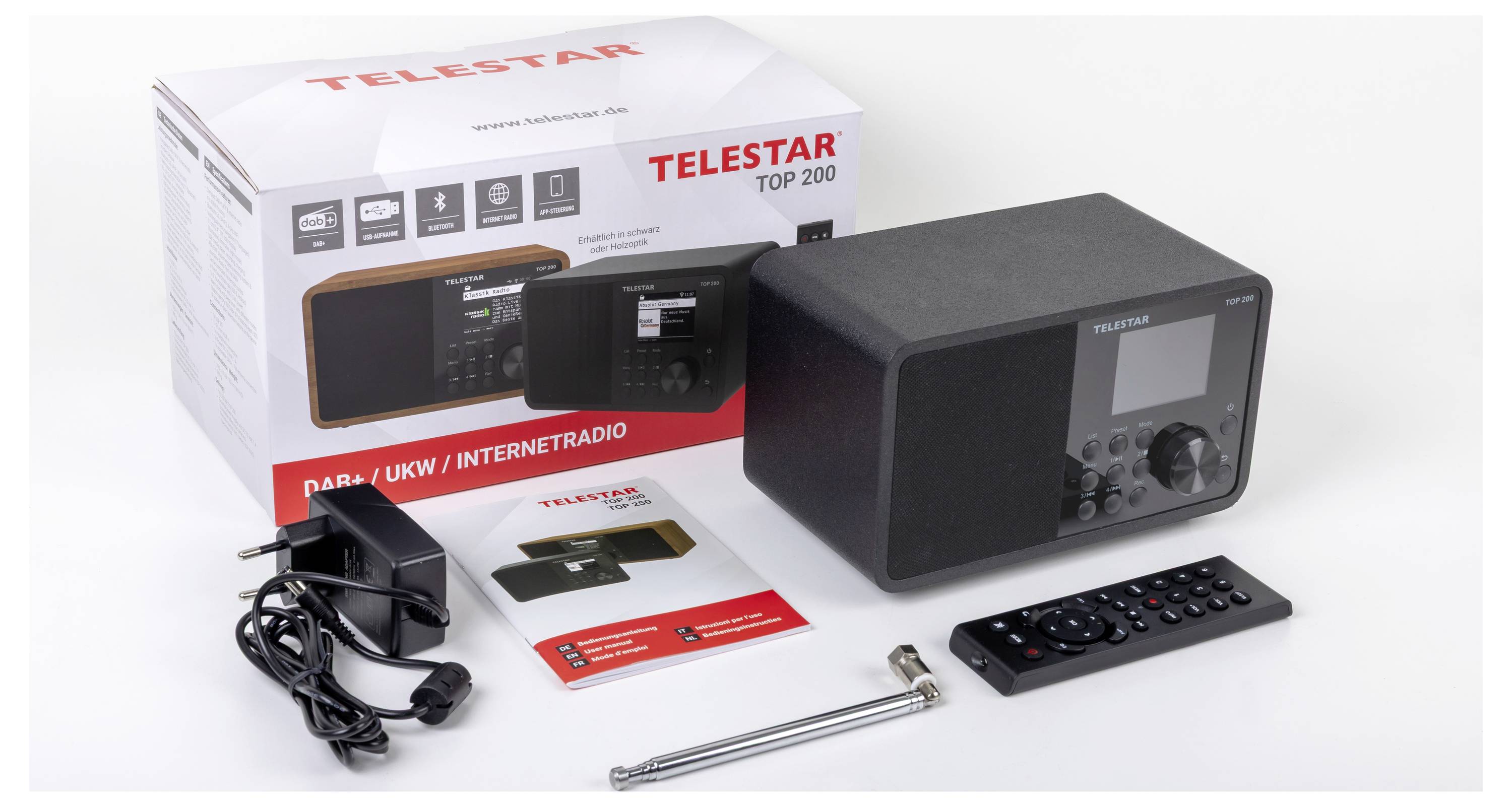 Čierne rádio TELSTAR je vystavené spolu so škatuľou, diaľkovým ovládačom, napájacím adaptérom, manuálom a anténou. Na škatuli je napísané 'TELSTAR TOP 200'.