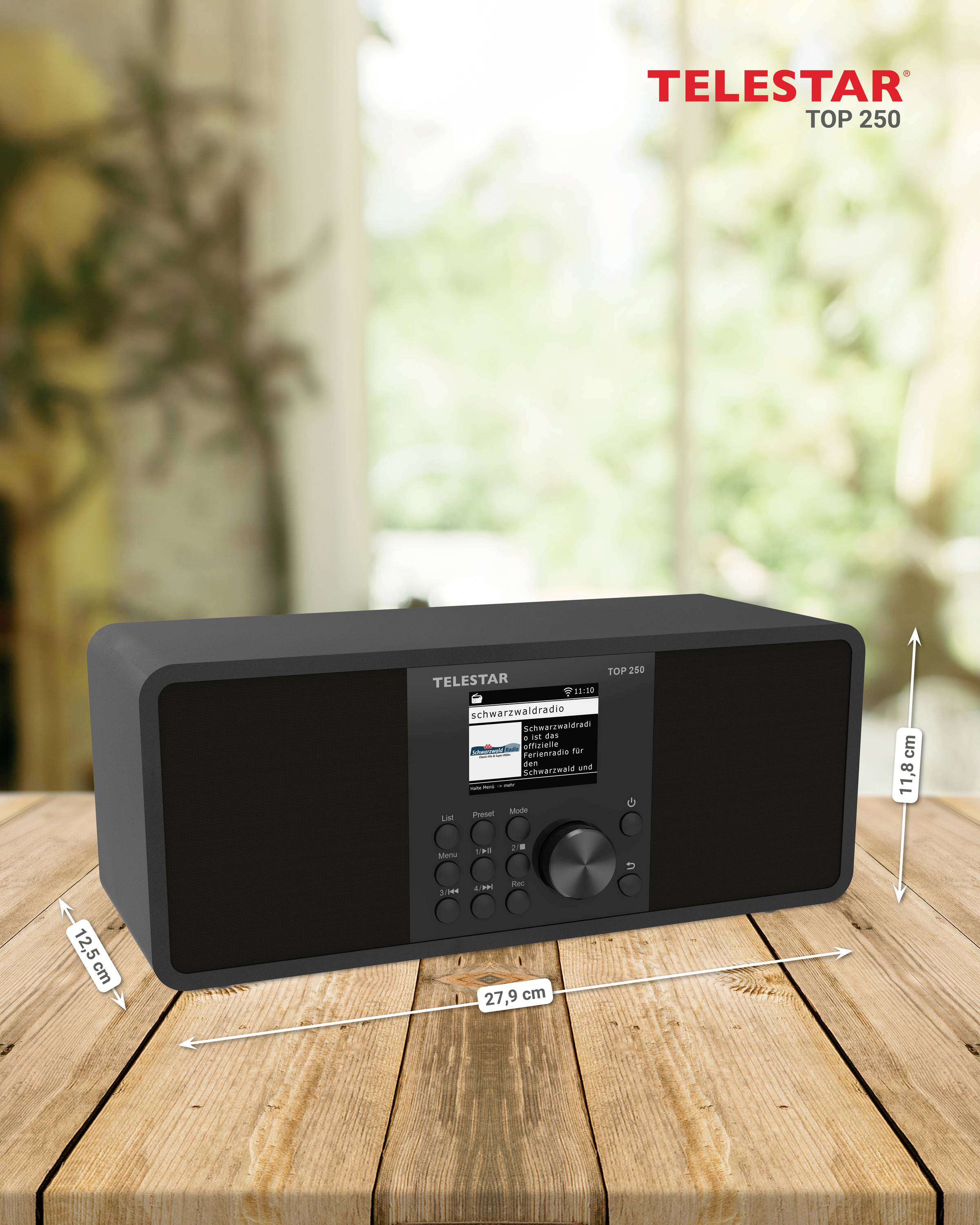 Rádio s digitálnym displejom stojí na dreveном stole. Rozmery sú 14,7 cm výšky, 27,9 cm šírky a 13,9 cm hĺbky. V pozadí rozmazaná príroda.