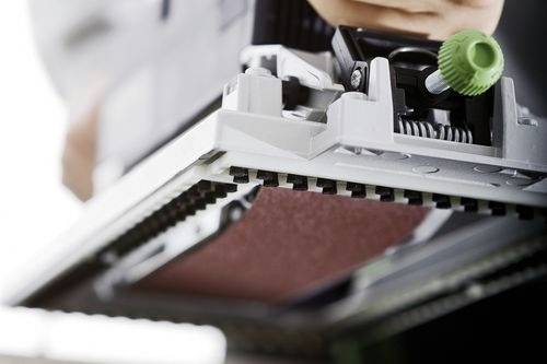 Ruka nastavuje zelený gombík na kancelárskom zariadení, zameriava sa na tonerový zásobník alebo súčasť tlačiarne, čo naznačuje údržbu alebo nastavenie.