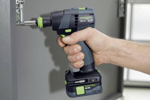 Osoba používajúca bezdrôtovú elektrickú vŕtačku na dotiahnutie skrutky na kovovom pántovom pripevnenom ku dverám skrinky. Vŕtačka je pevne držaná v ruke.