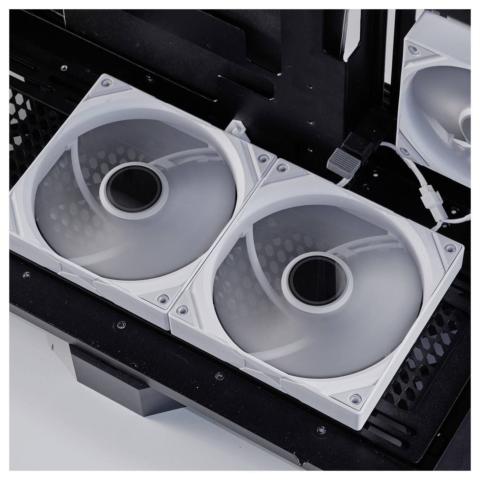 Dva biele chladiace ventilátory nainštalované v počítačovej skrinke, umiestnené vedľa seba, pričom tretí ventilátor je čiastočne viditeľný v pozadí.