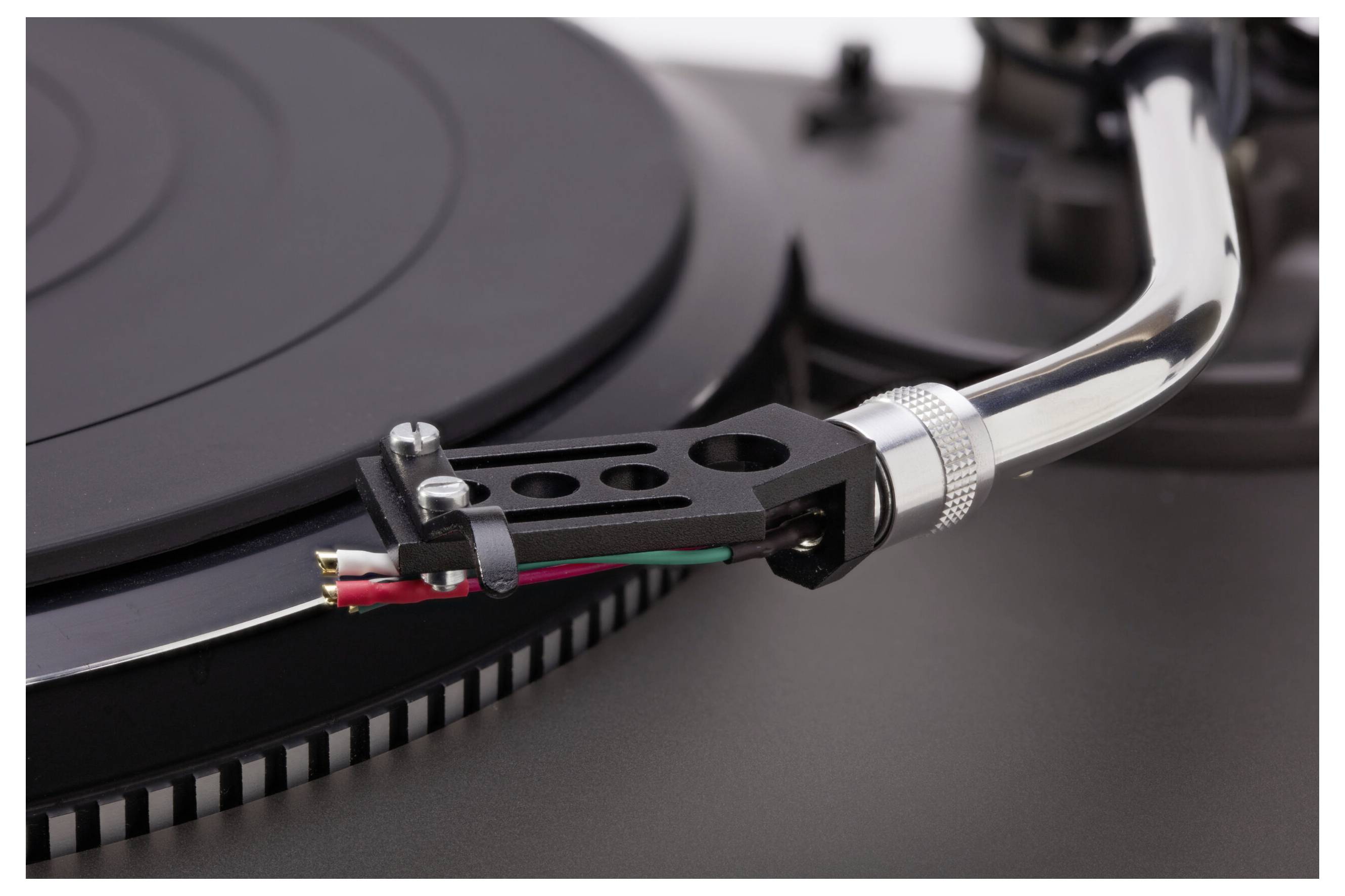 Detail záberník gramofónu, ktorého rameno sa vznáša nad vinylovou platňou, pričom zvýrazňuje komplexný dizajn a zapojenie držiaka prenosky.