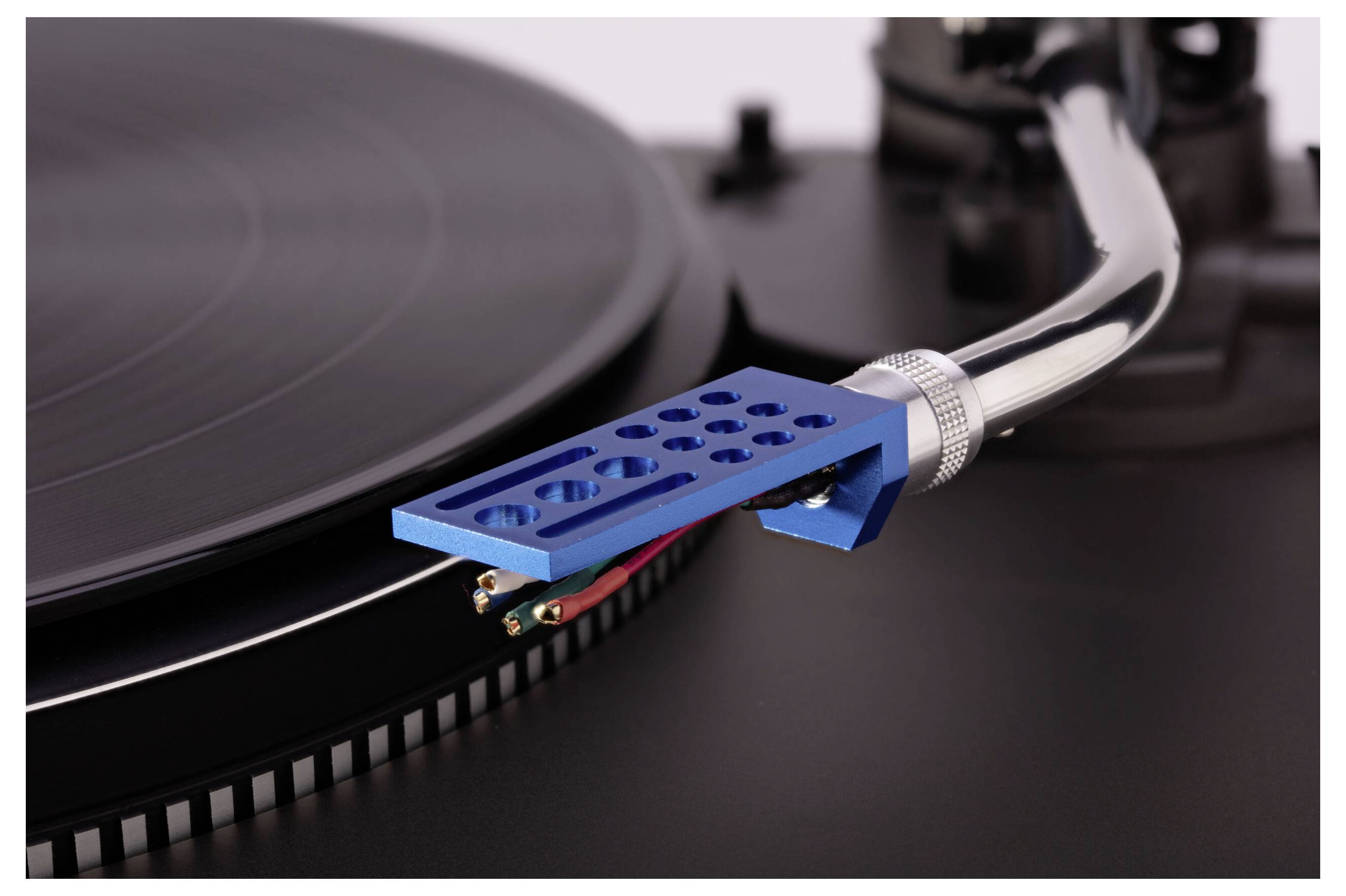 Detailný záber gramofónu s modrou ramienkou, ktorý prehráva vinylový záznam, so zameraním na ihlu a drážky, zvýrazňujúci vintage audio zariadenie.