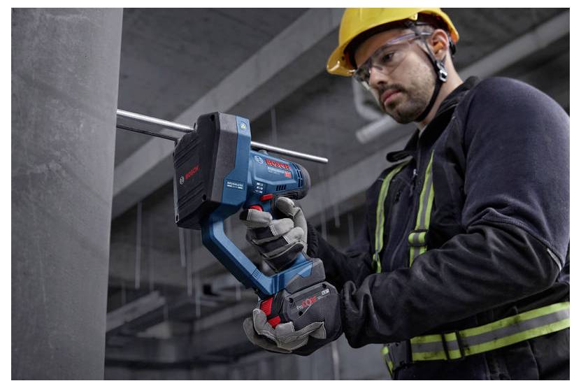 Stavebný robotník v bezpečnostnej výbave používa aku-vŕtačku Bosch na vŕtanie do betónovej pilóny v priemyselnom prostredí.