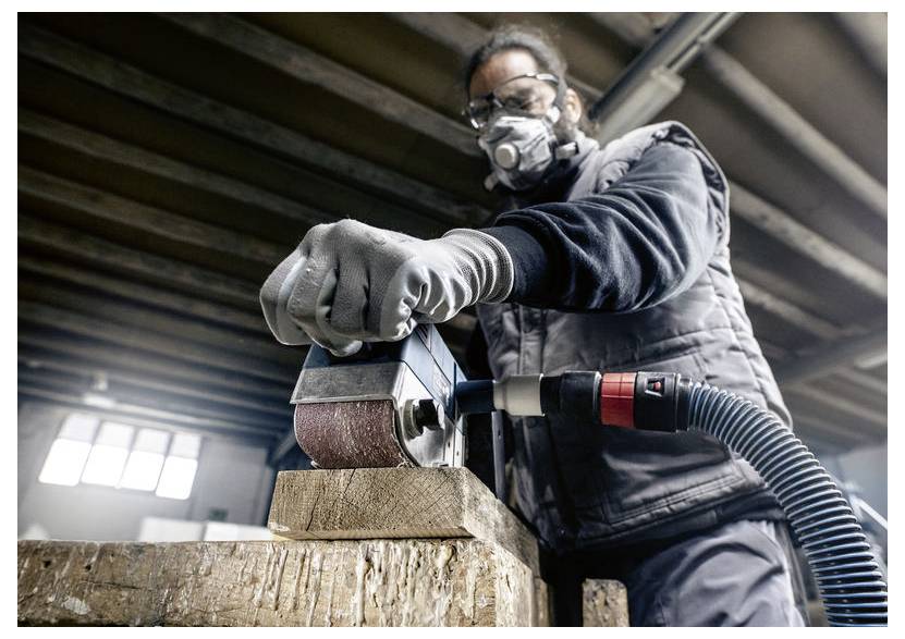 Osoba v ochrannom oblečení obsluhuje vibračnú brúsku na drevenej ploche v dielni. Pripojený systém na zber prachu.