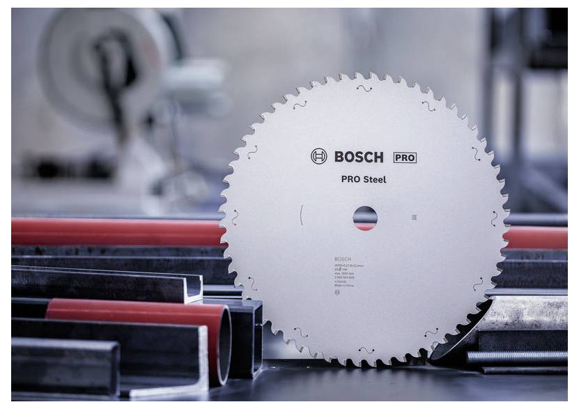 Kotúčová píla s nápisom "BOSCH PRO Steel" je umiestnená vzpriamene medzi rôznymi kovovými potrubiami, čo naznačuje priemyselné využitie.