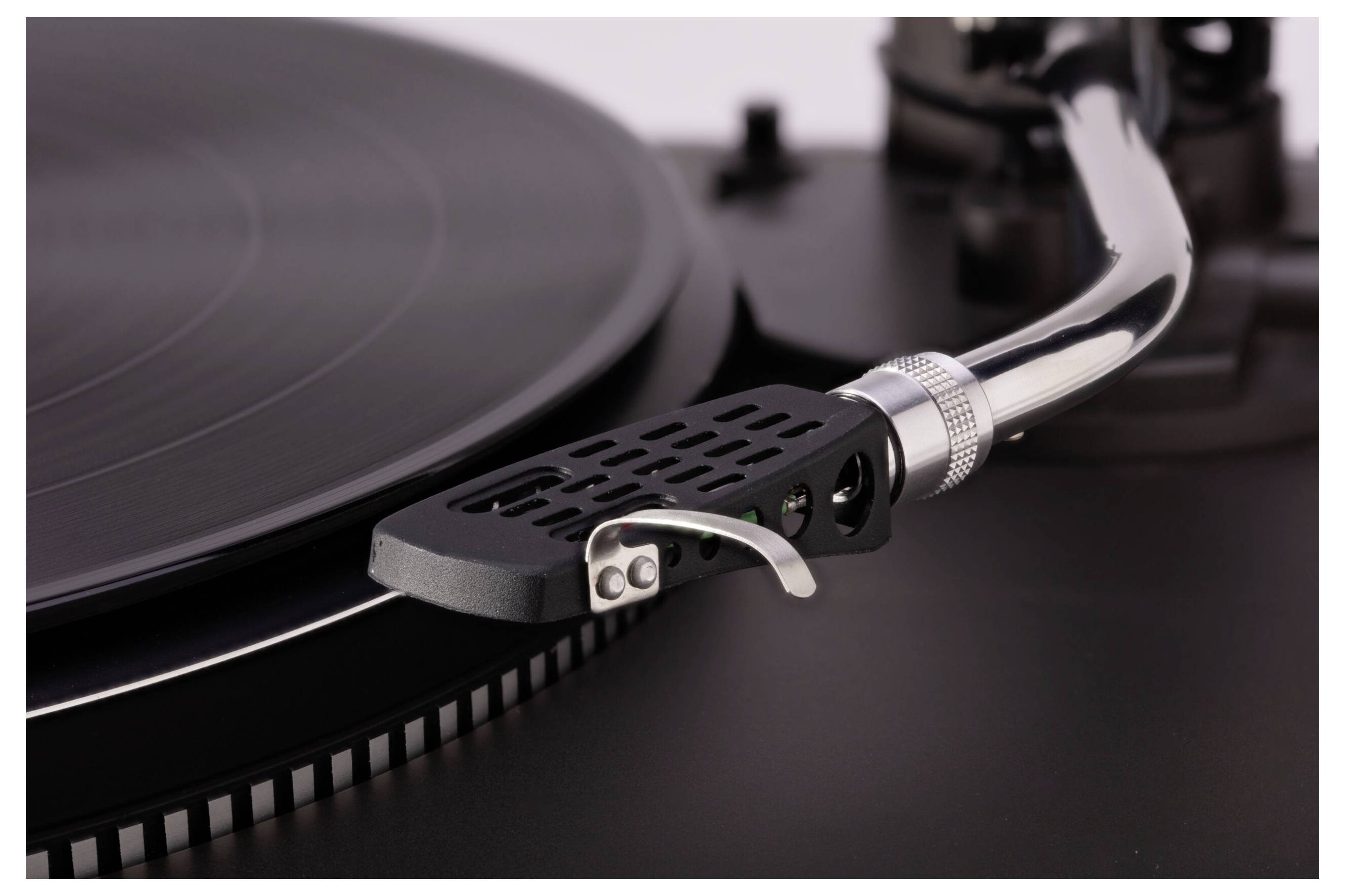 Detailný záber ihly a ramena gramofónu spočívajúcich na vinylového platni, zvýrazňujúci drážky a detaily prehrávača platní.