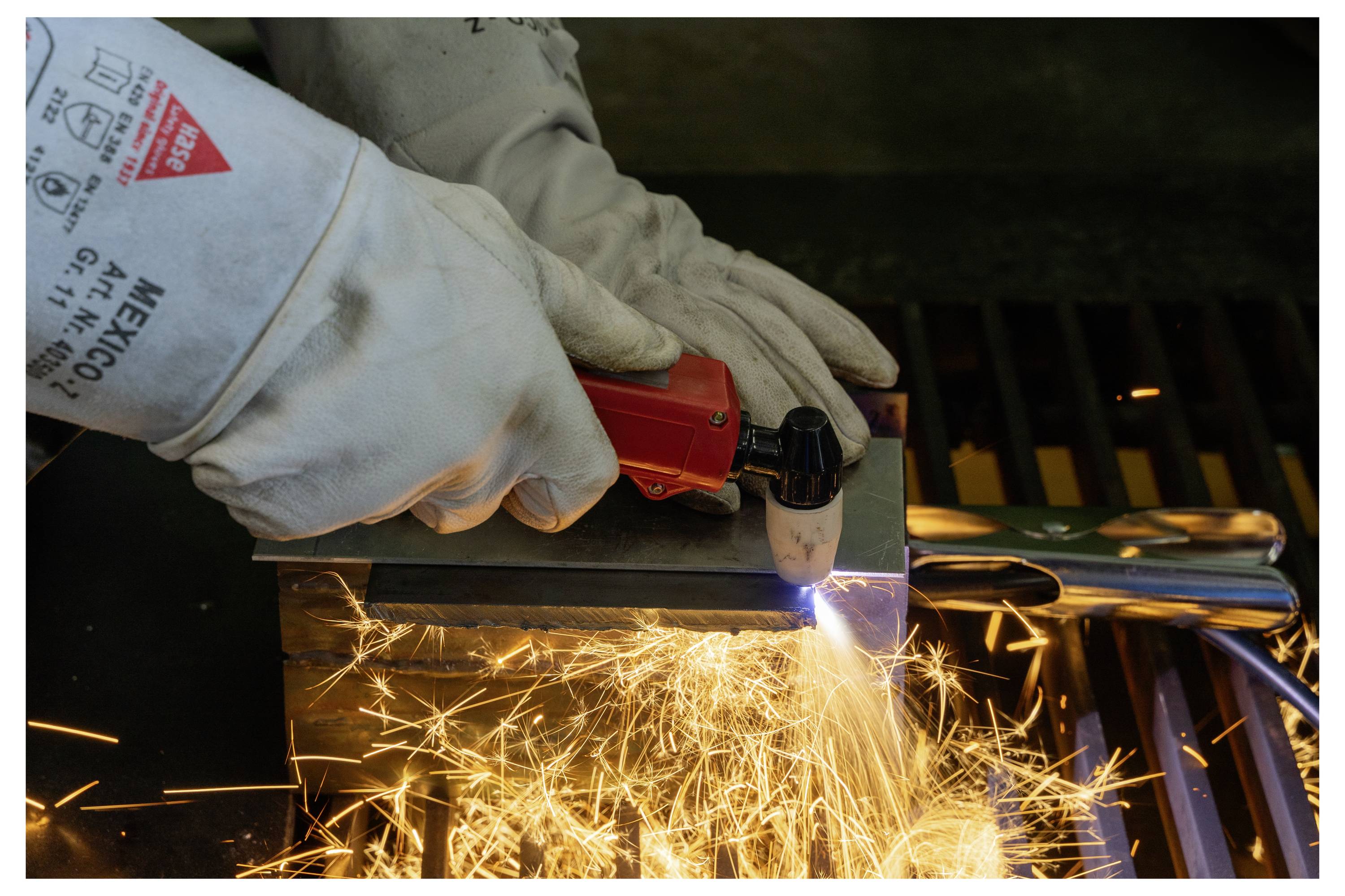 Rukavicami chránené ruky používajú plazmový rezací stroj na kovovom plechu, pričom spôsobujú jasné iskry lietajúce do priestoru. Tento proces je súčasťou spracovania kovov alebo výroby.