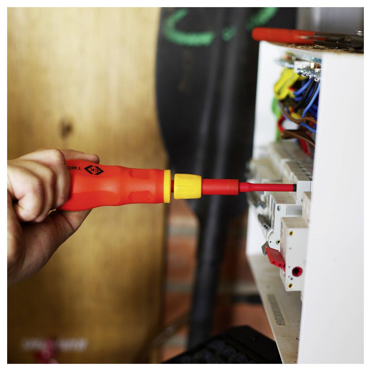 Osoba používa izolovaný skrutkovač pri práci na poistkovej skrinke so zameraním na elektrické vedenie. Scéna zvýrazňuje elektrotechnickú prácu a bezpečnostné nástroje.